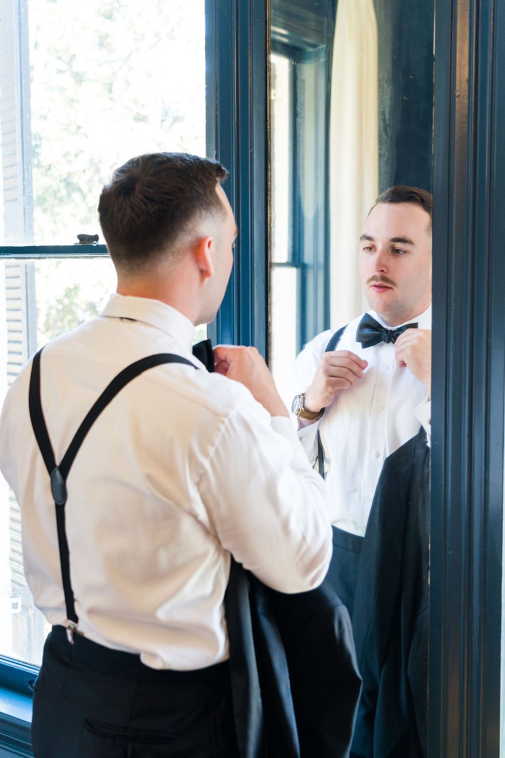 Person adjusting bow tie while looking in mirror with navy blue trim.