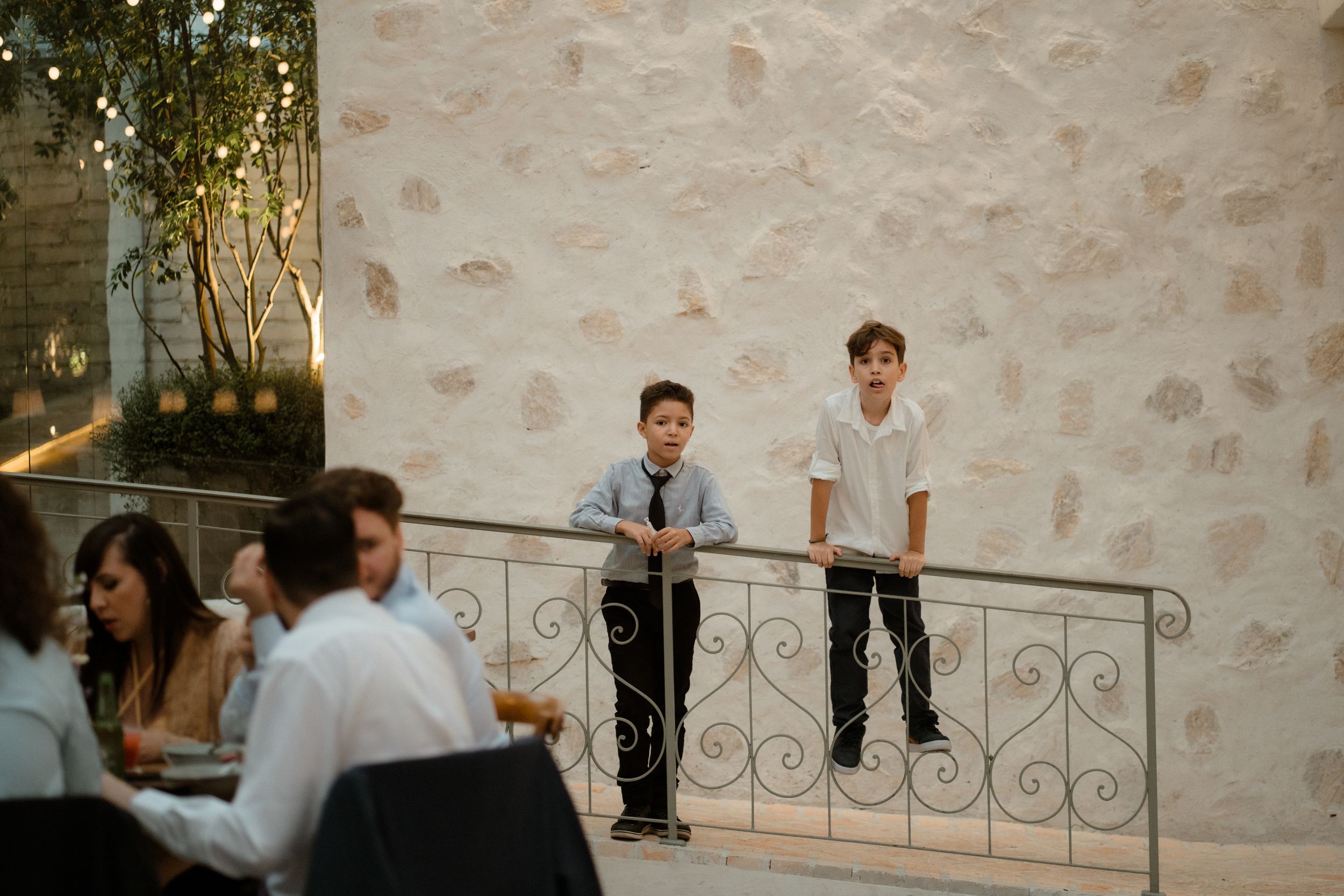 Two kids watching from a balcony during a wedding event.