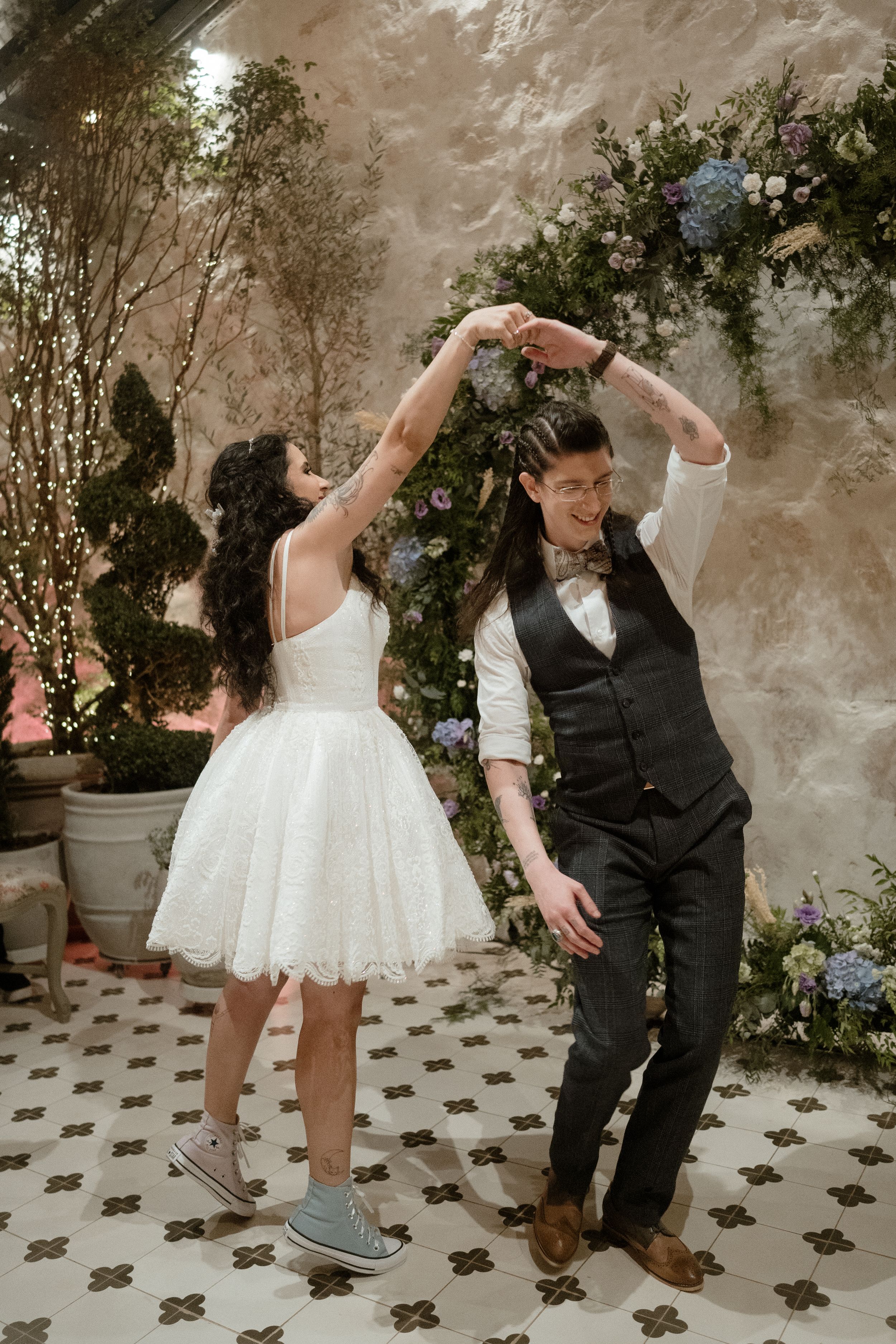 Couple dancing playfully among floral decorations at a wedding.