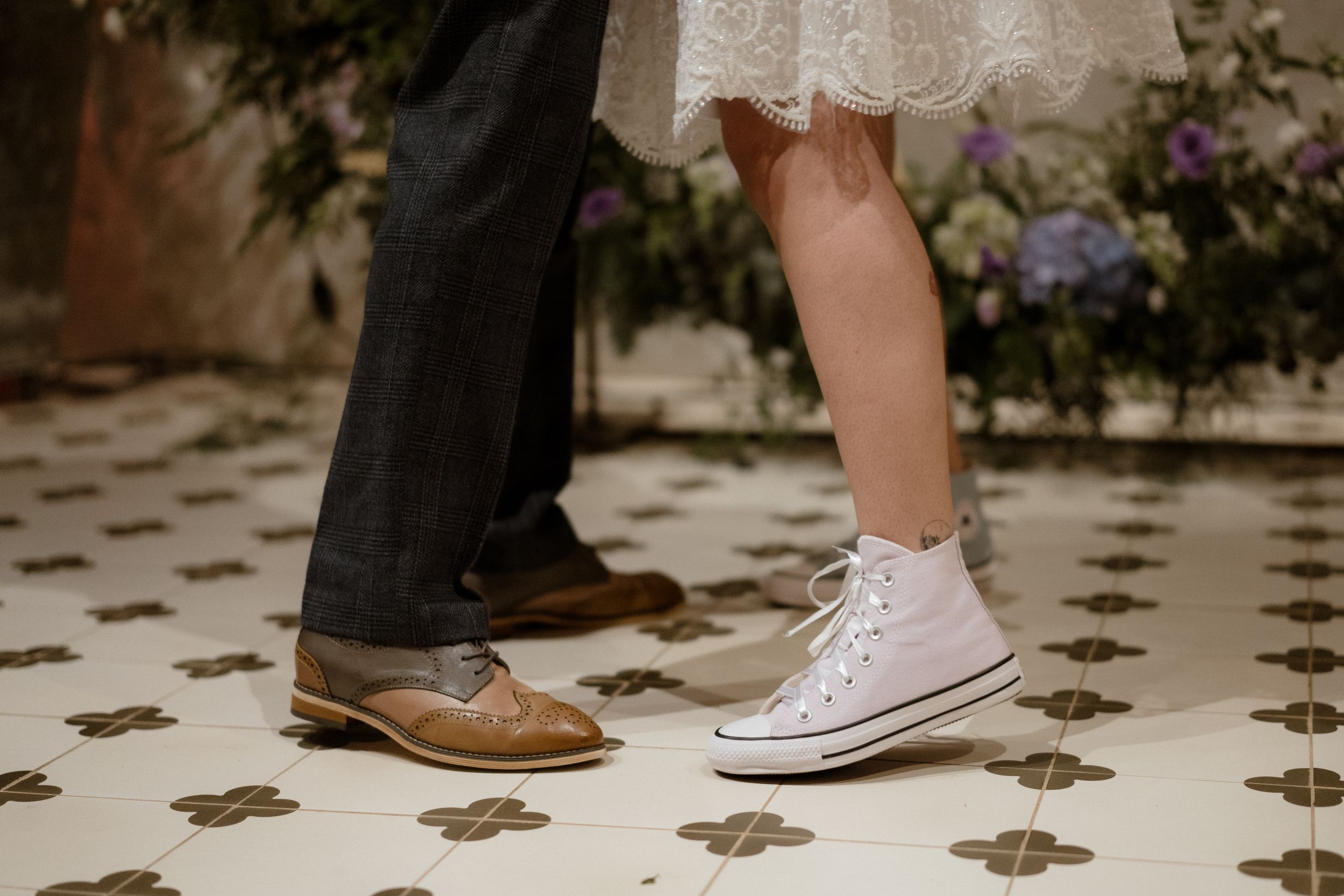 Close-up of formal dress shoes and sneakers on a patterned floor.