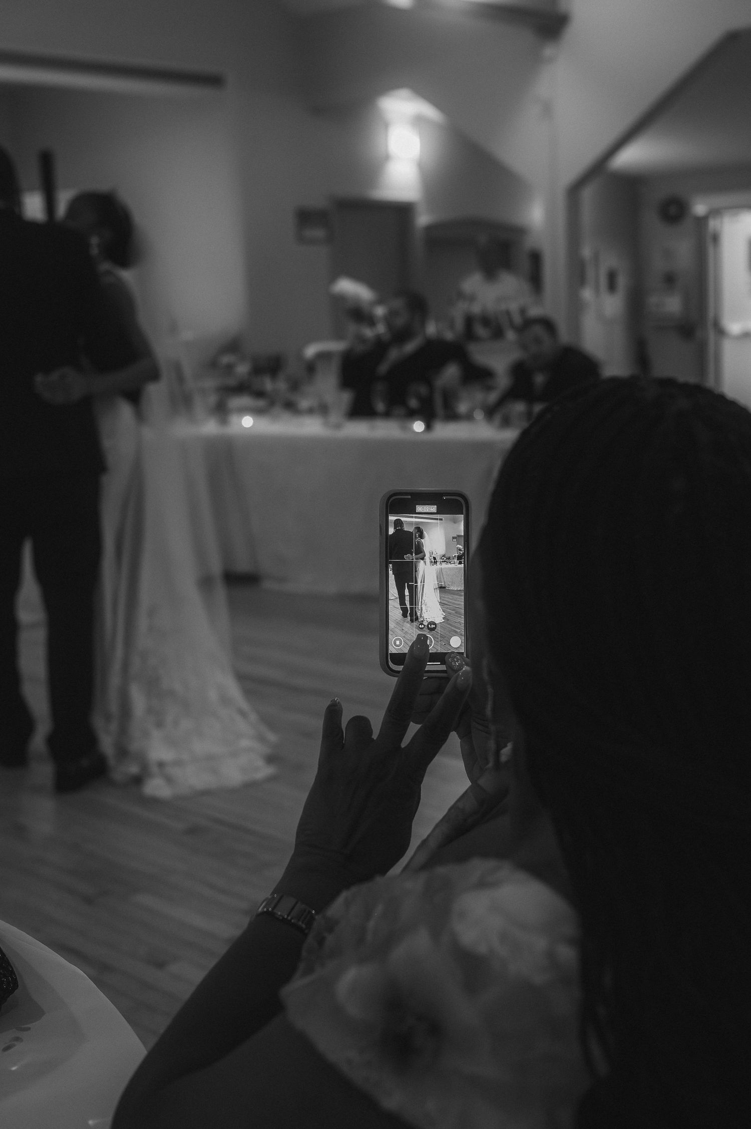 Guest capturing wedding reception moment on smartphone in black and white.