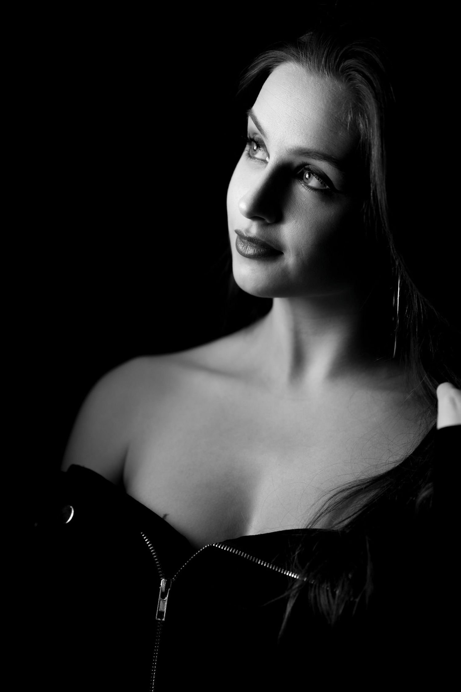 Black and white low-key portrait of a blonde woman in an off-shoulder leather top.