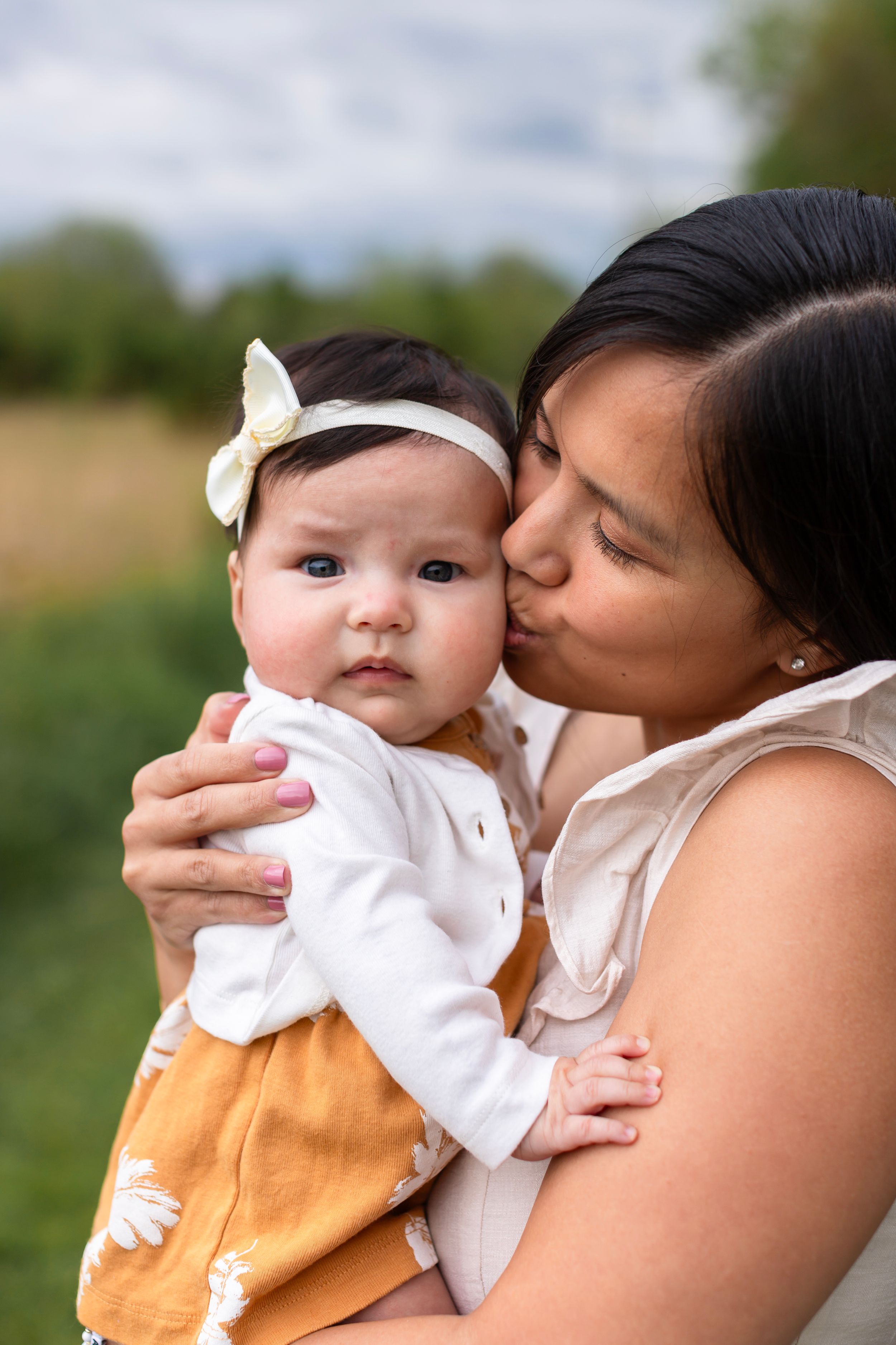 A tender moment between parent and baby wearing a white bow headband outdoors.