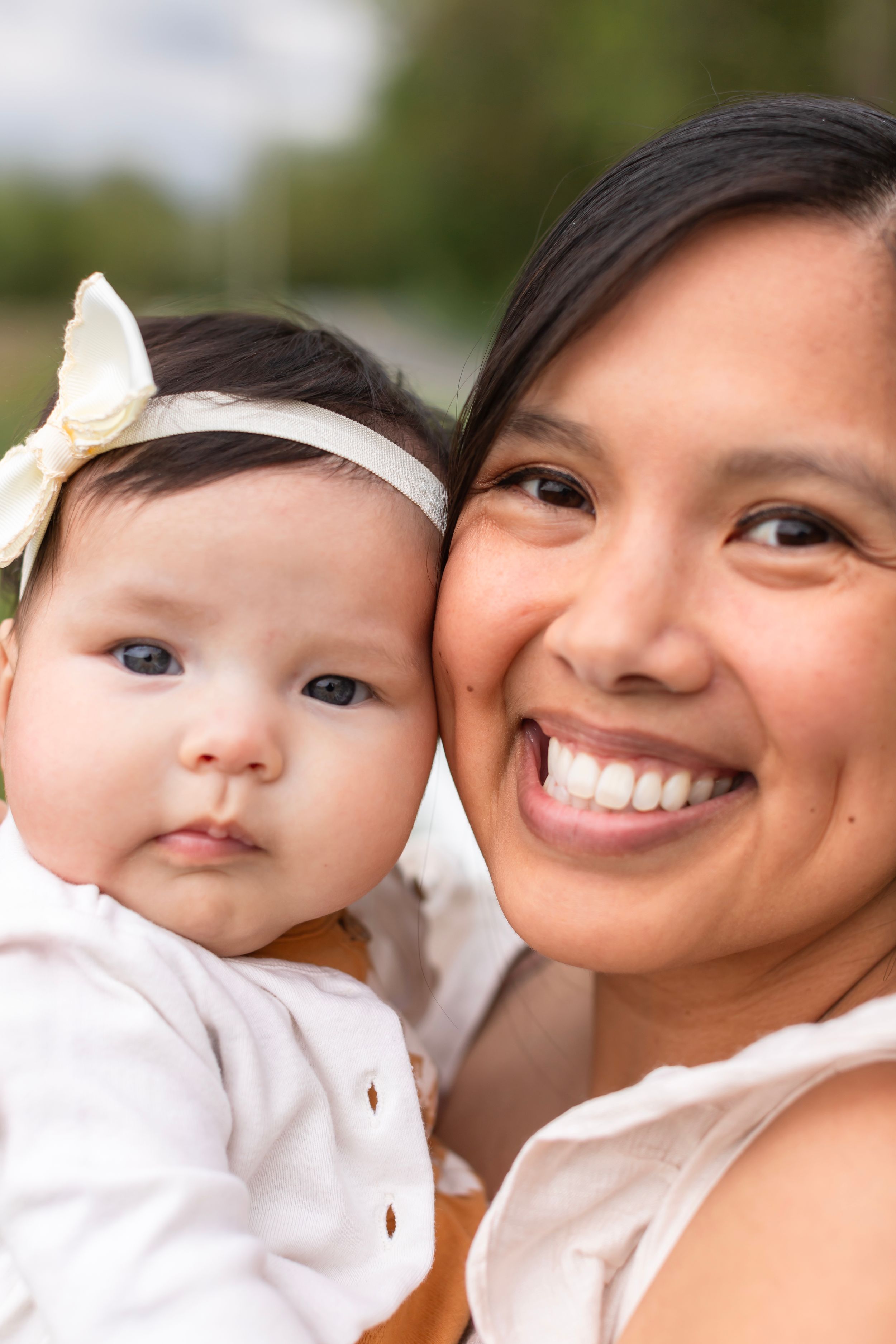A close-up portrait of parent and baby with matching white outfits against a natural backdrop.