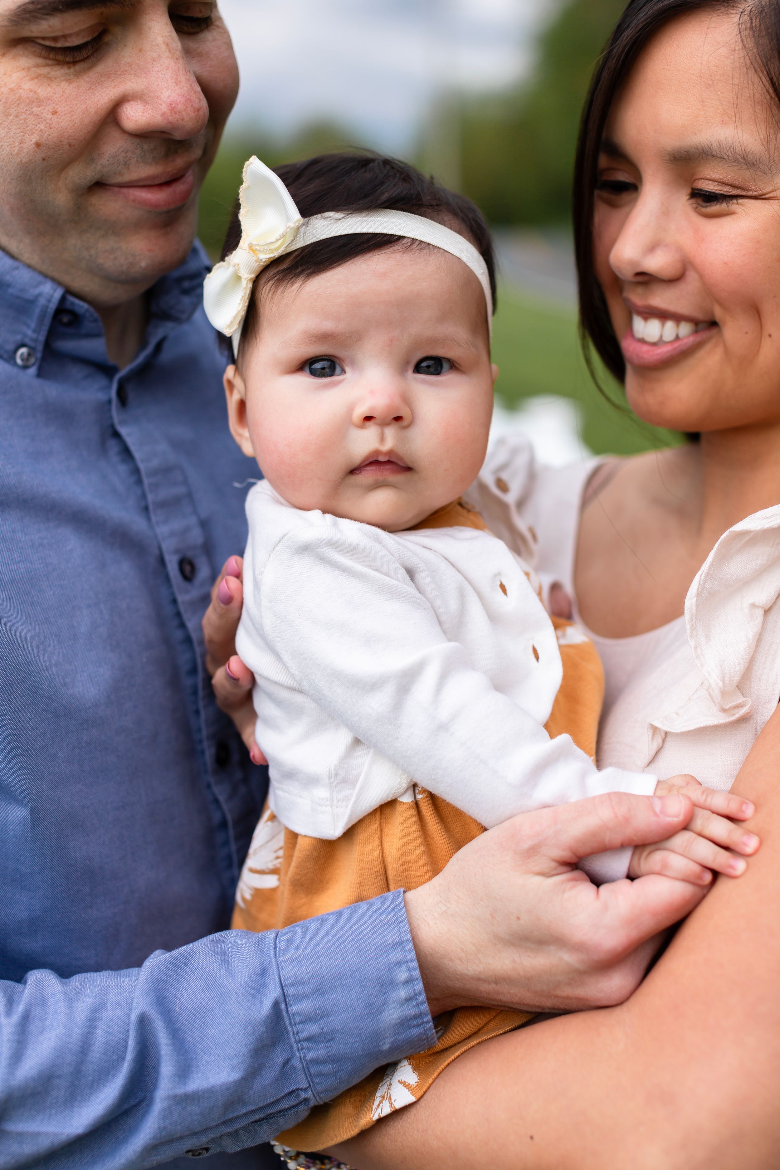 A family shares an intimate moment together outdoors with their baby in white and yellow attire.