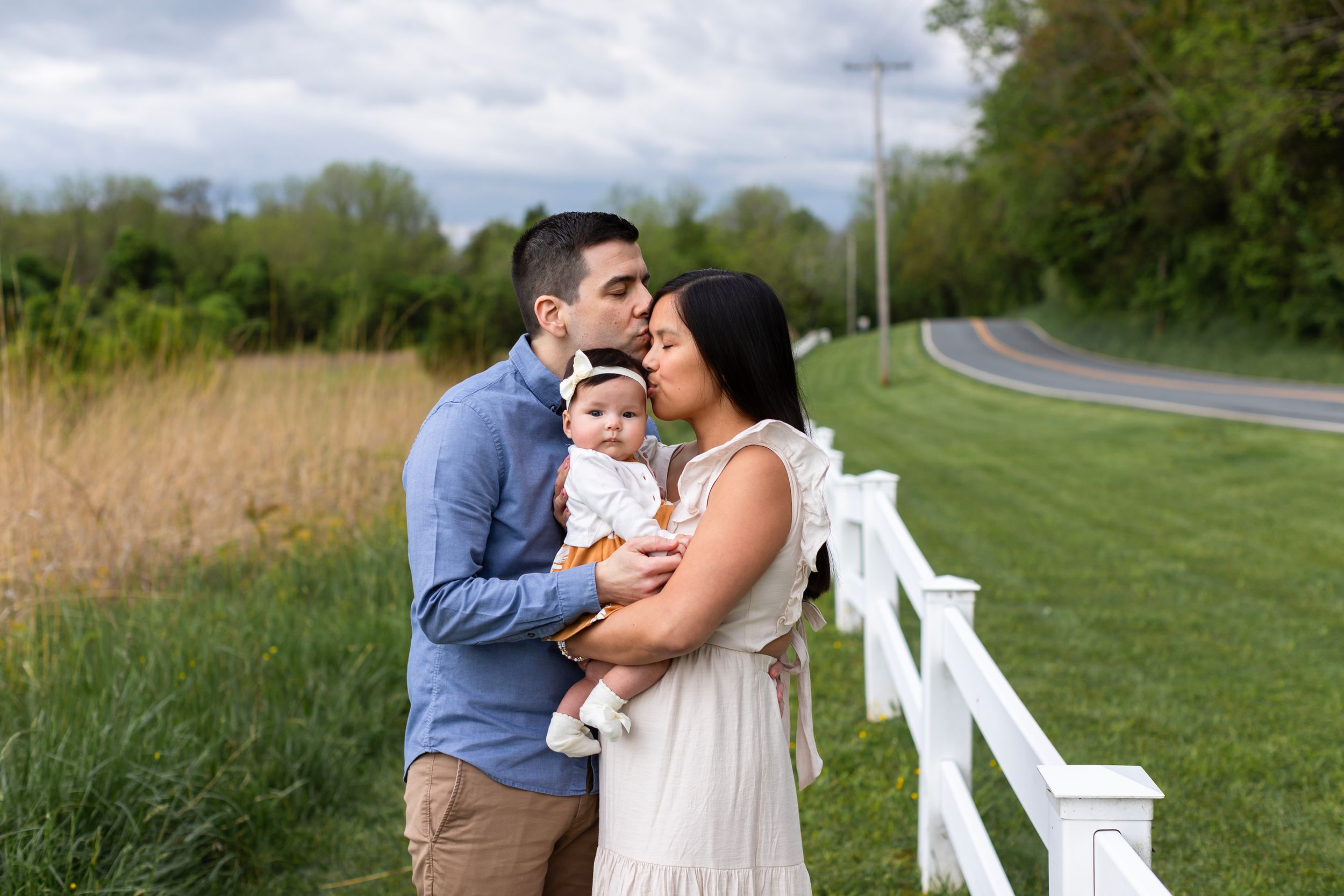 A family embraces near a white fence with rolling countryside in the background.