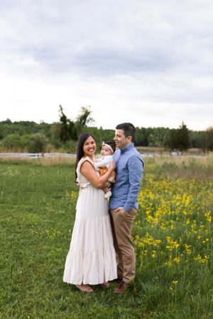 Family standing together in field of yellow wildflowers during outdoor photo session.