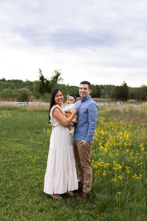 A family enjoys a spring day together in a field of yellow wildflowers with trees and water in the background.