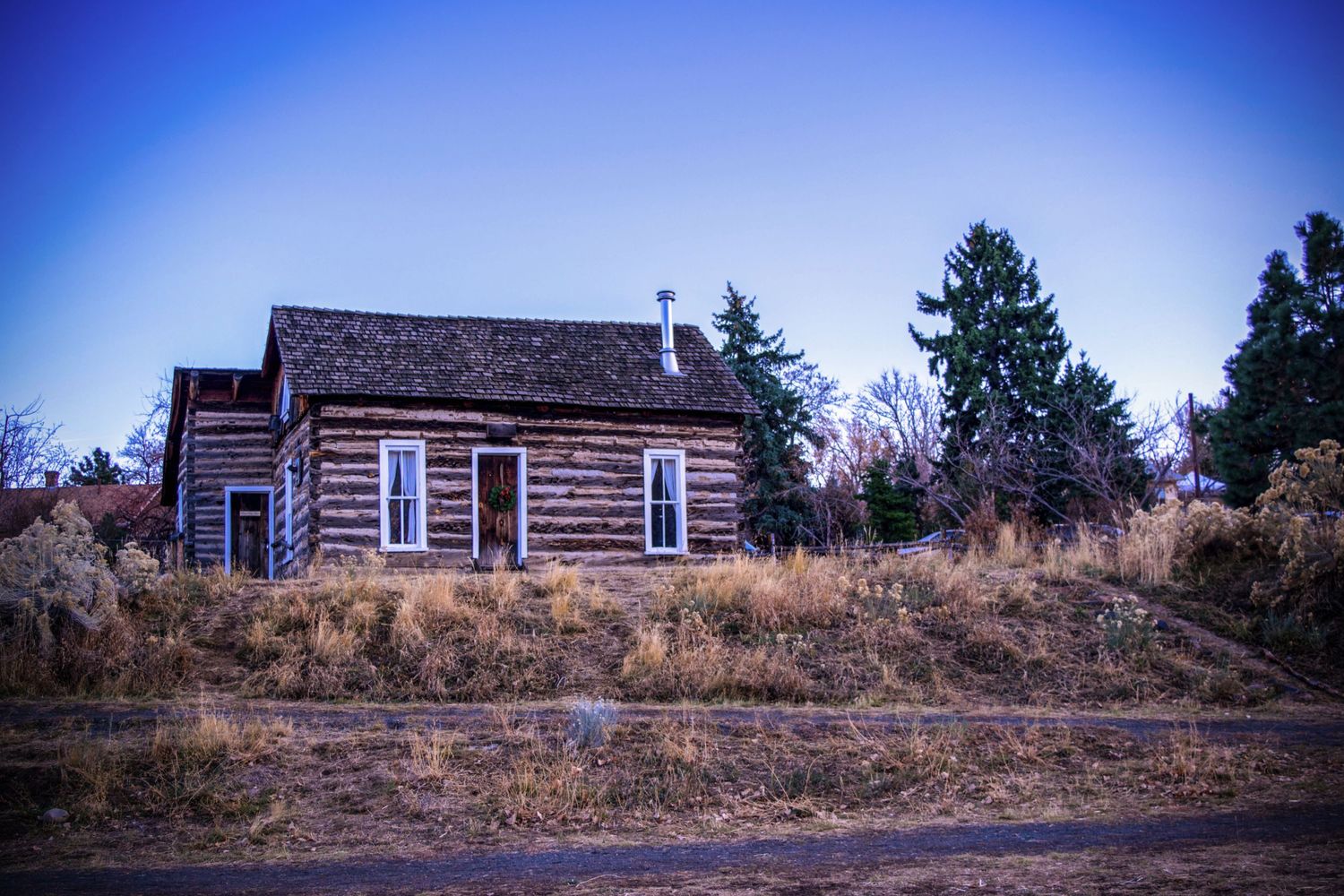 Rustic wooden cabin stands alone on a hillside against bright blue sky.