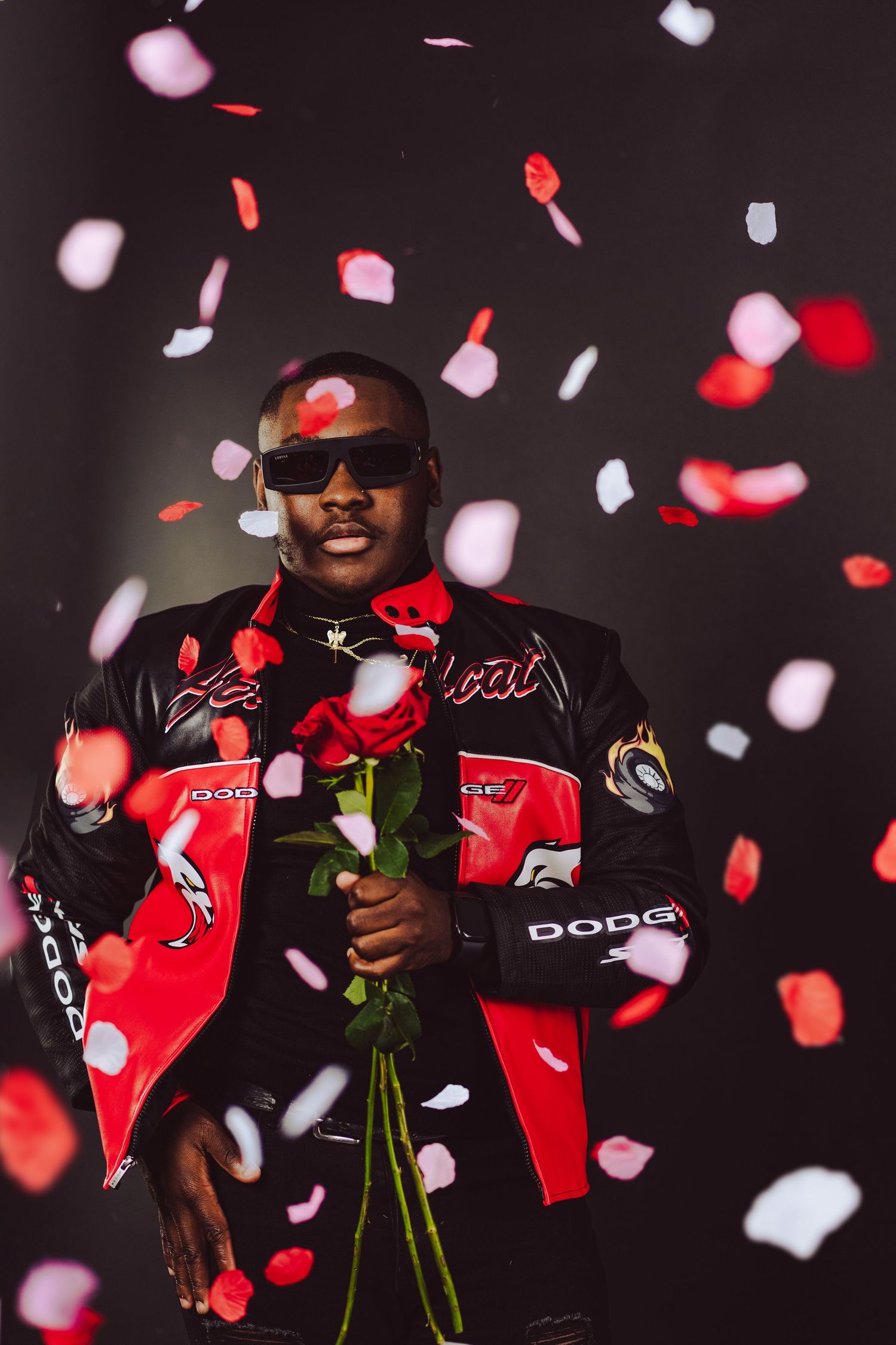 Person in red and black jacket holding roses while rose petals fall in the background.