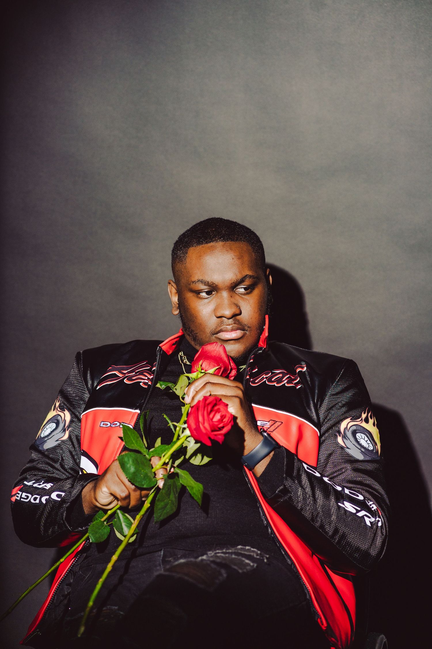 Portrait of person in black leather jacket holding red roses against gray background.