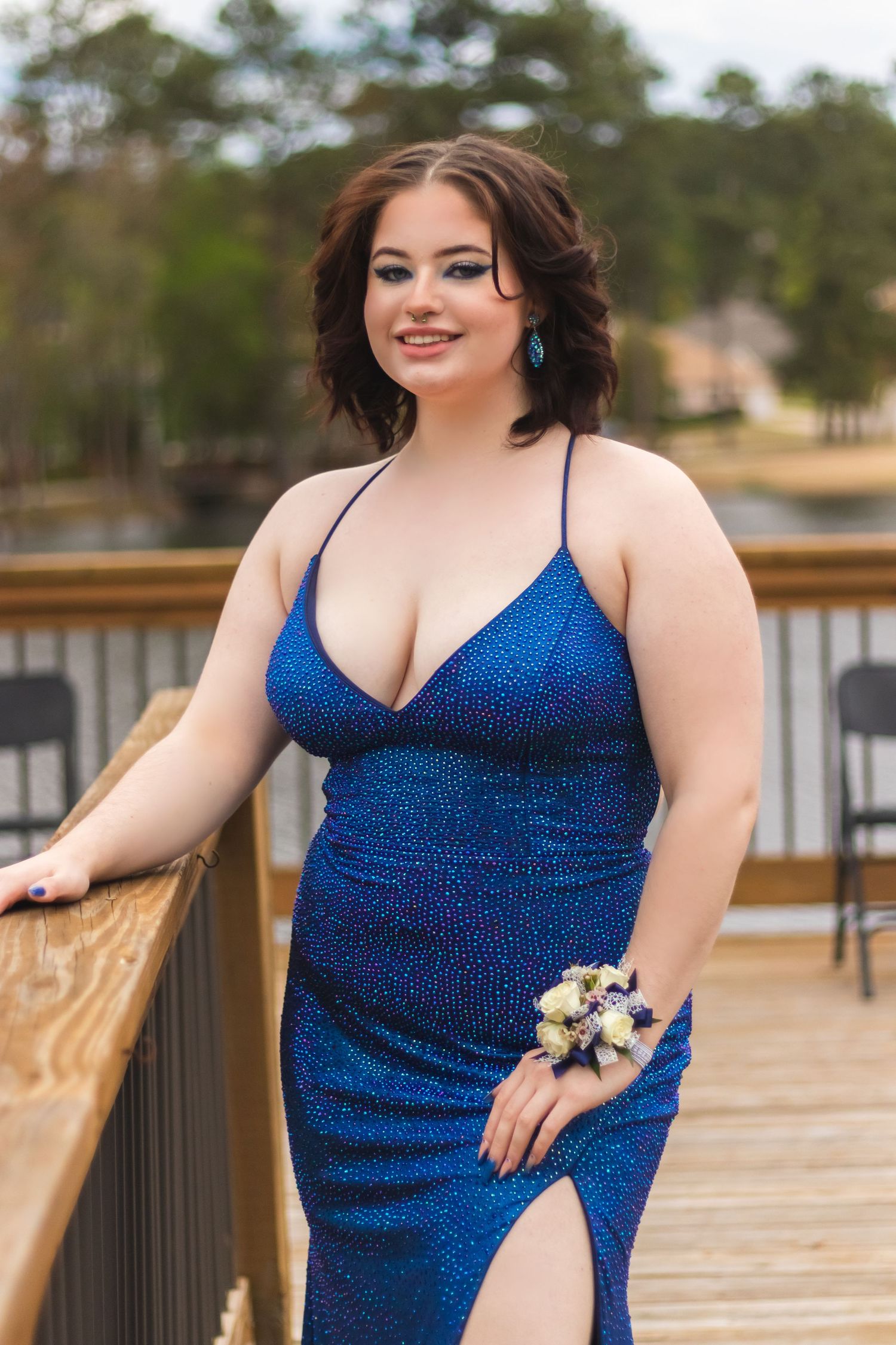 Woman in sparkling blue formal dress poses with corsage on wooden boardwalk.