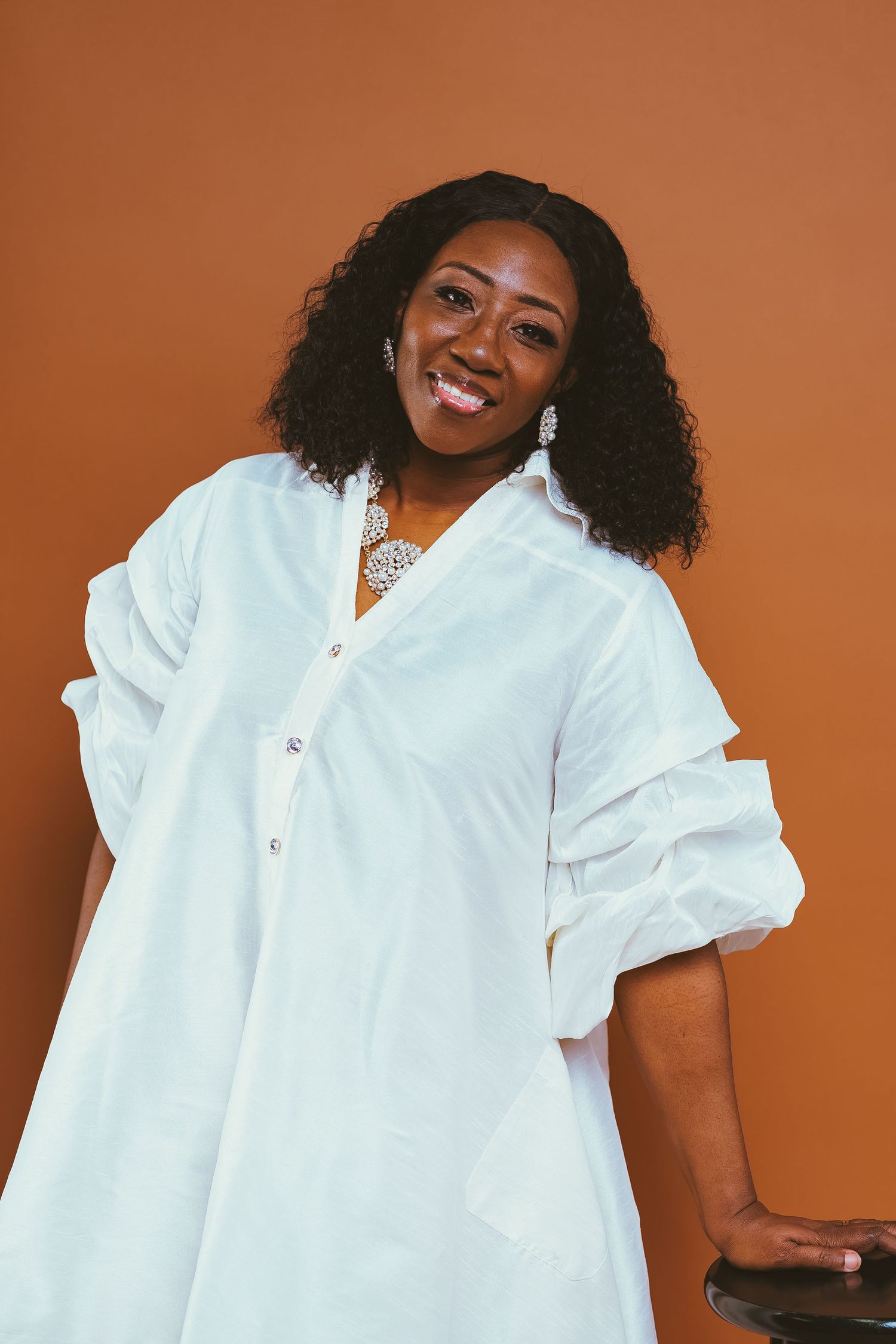 A portrait of someone wearing a flowing white dress against a brown background.