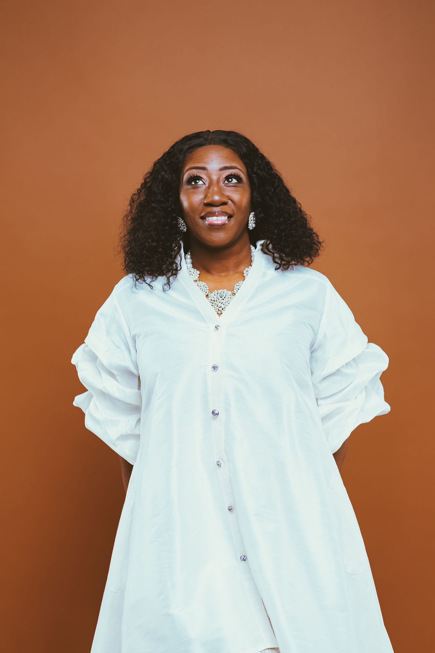 A fashion portrait featuring a white button-down dress with statement jewelry.