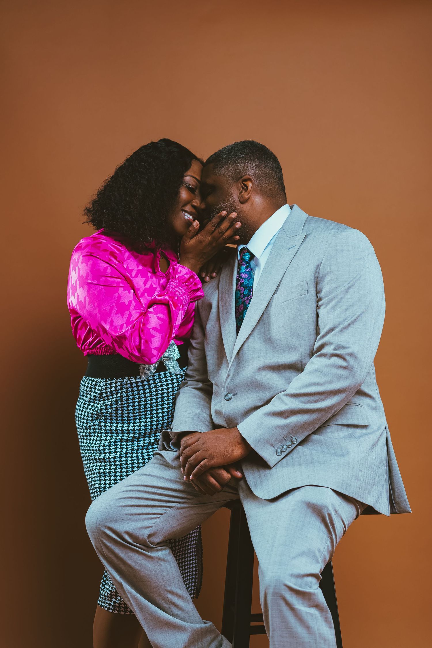 A couple in formal attire sharing an intimate moment against a brown background.