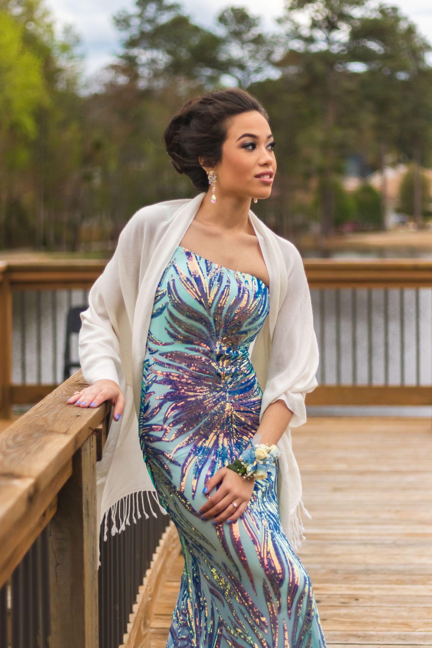Woman in elegant floral print dress and white cardigan poses on wooden deck.