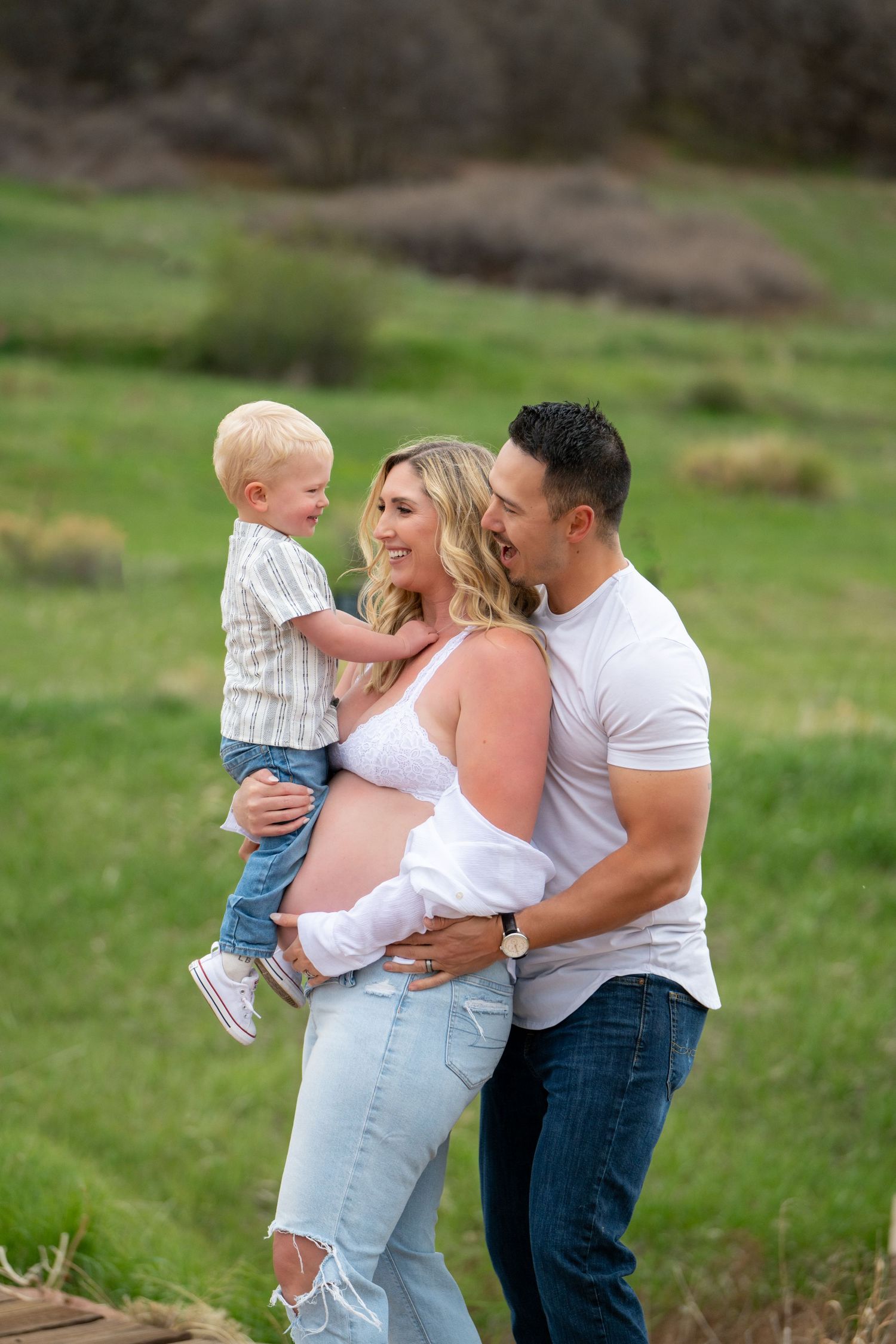 A family shares an intimate moment at sunset near a lake with fall foliage overhead.