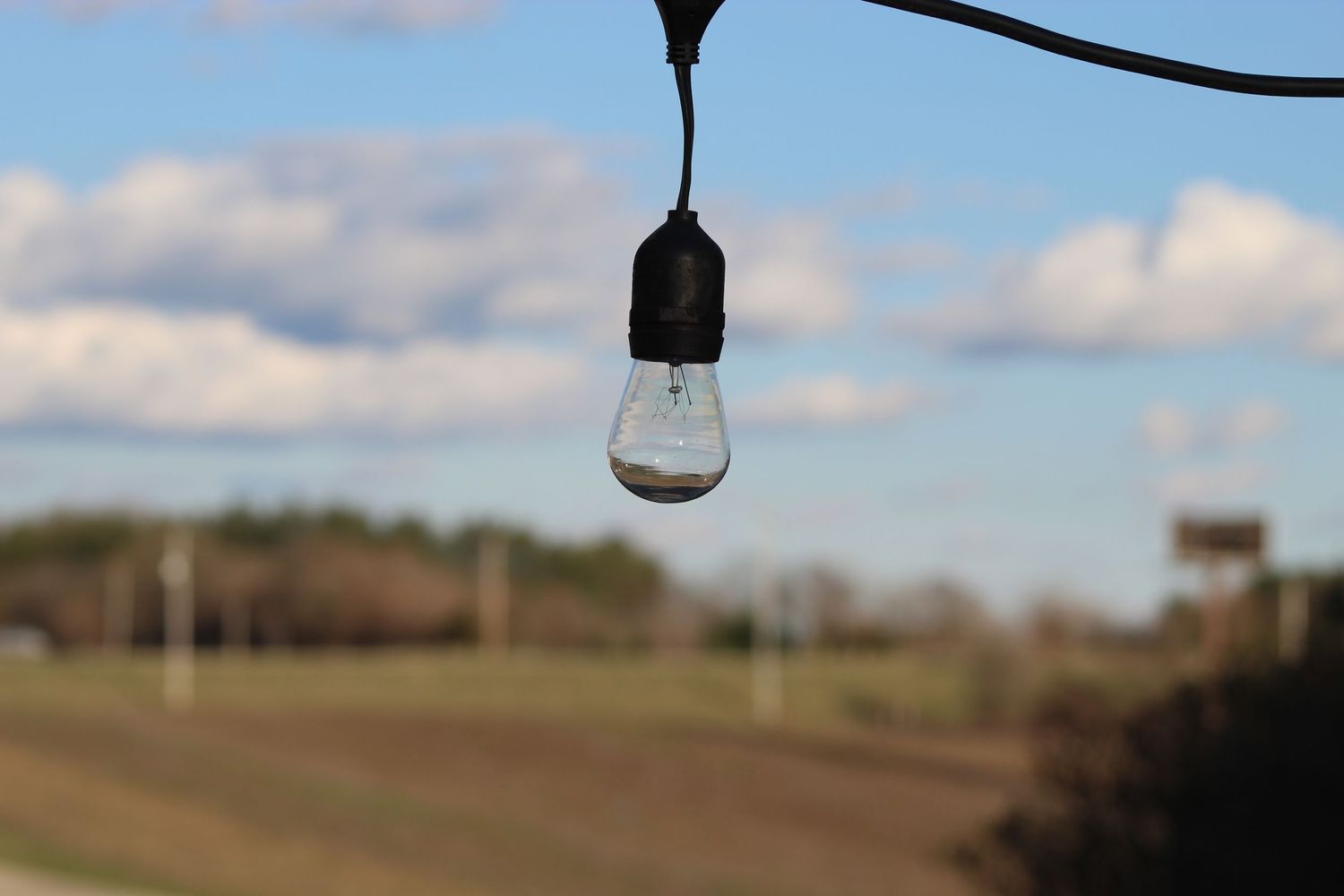 Scenic outdoor landscape with green fields and cloudy skies featuring a suspended lightbulb in view.