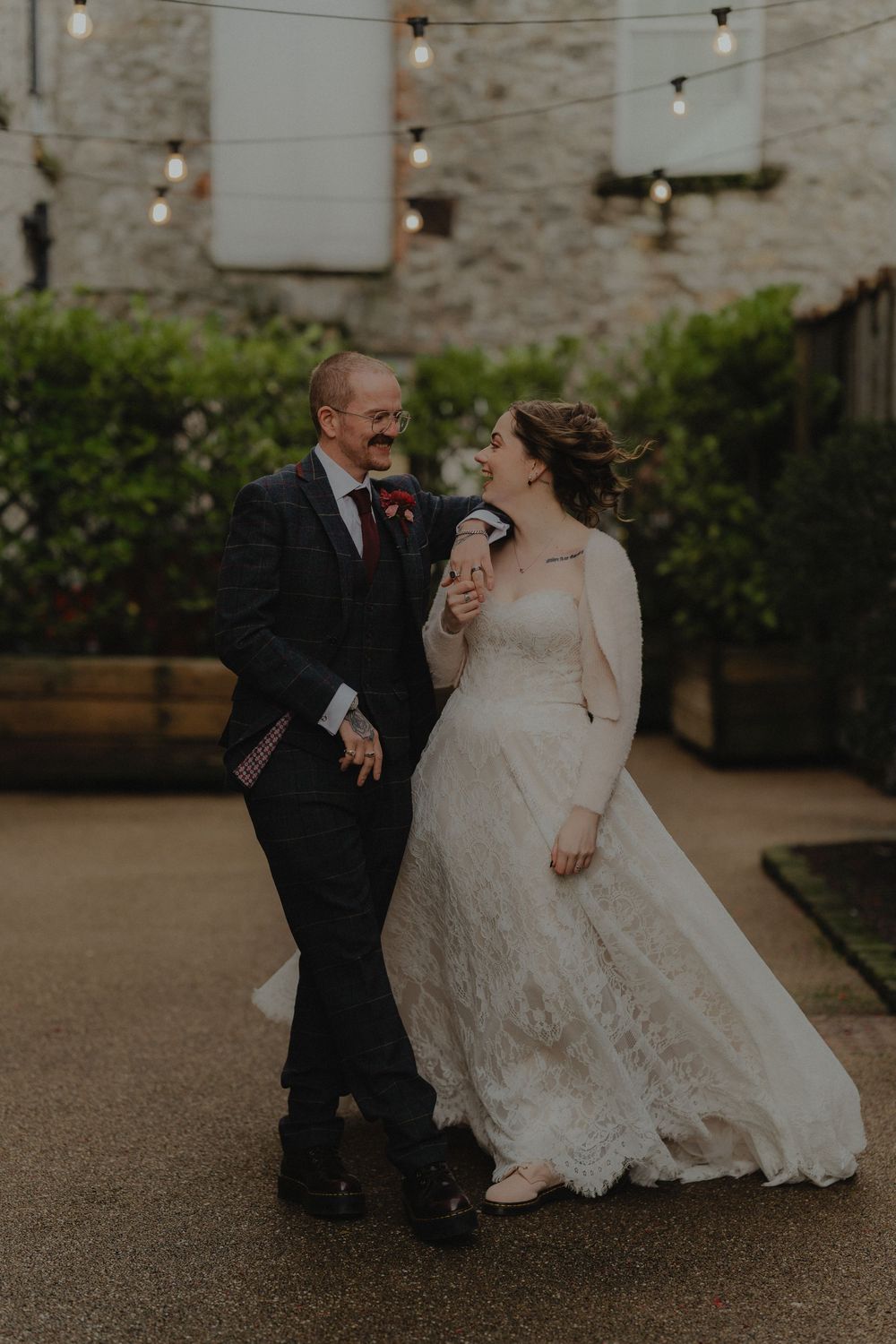 Bride and groom share a joyful moment dancing in a courtyard with string lights at their wedding.