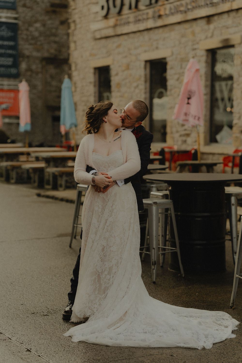 Bride and groom share a romantic kiss outside a rustic stone building on their wedding day.