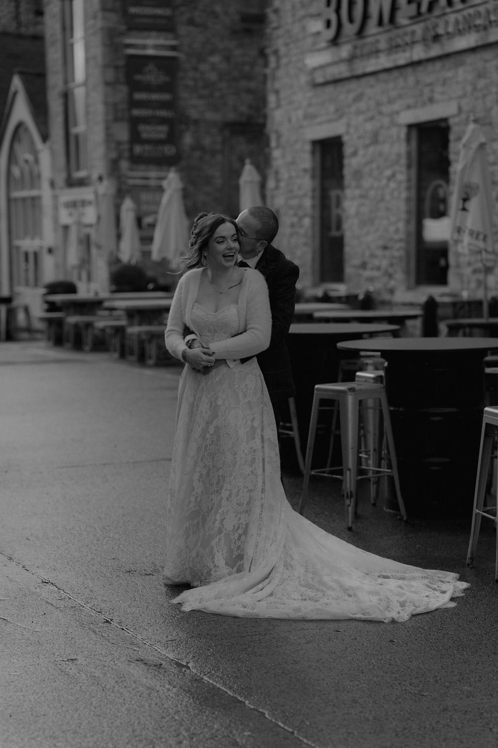 Black and white photo of a bride and groom sharing a tender moment outside a rustic brick building.