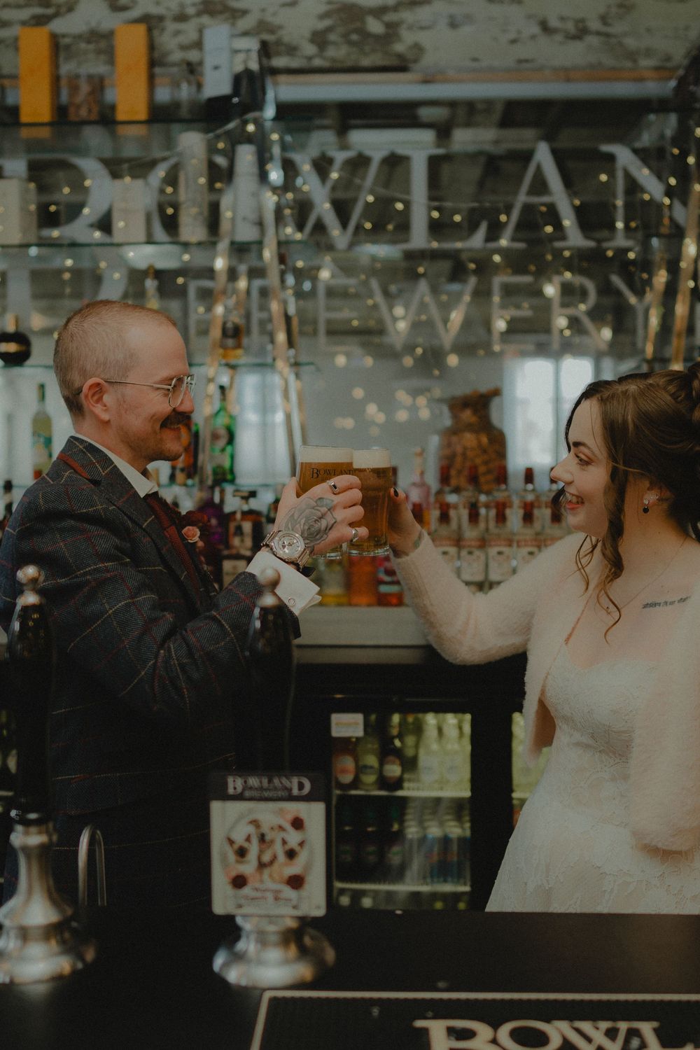 Bride and groom toasting with beer glasses at Bowland Brewery bar on their wedding day.