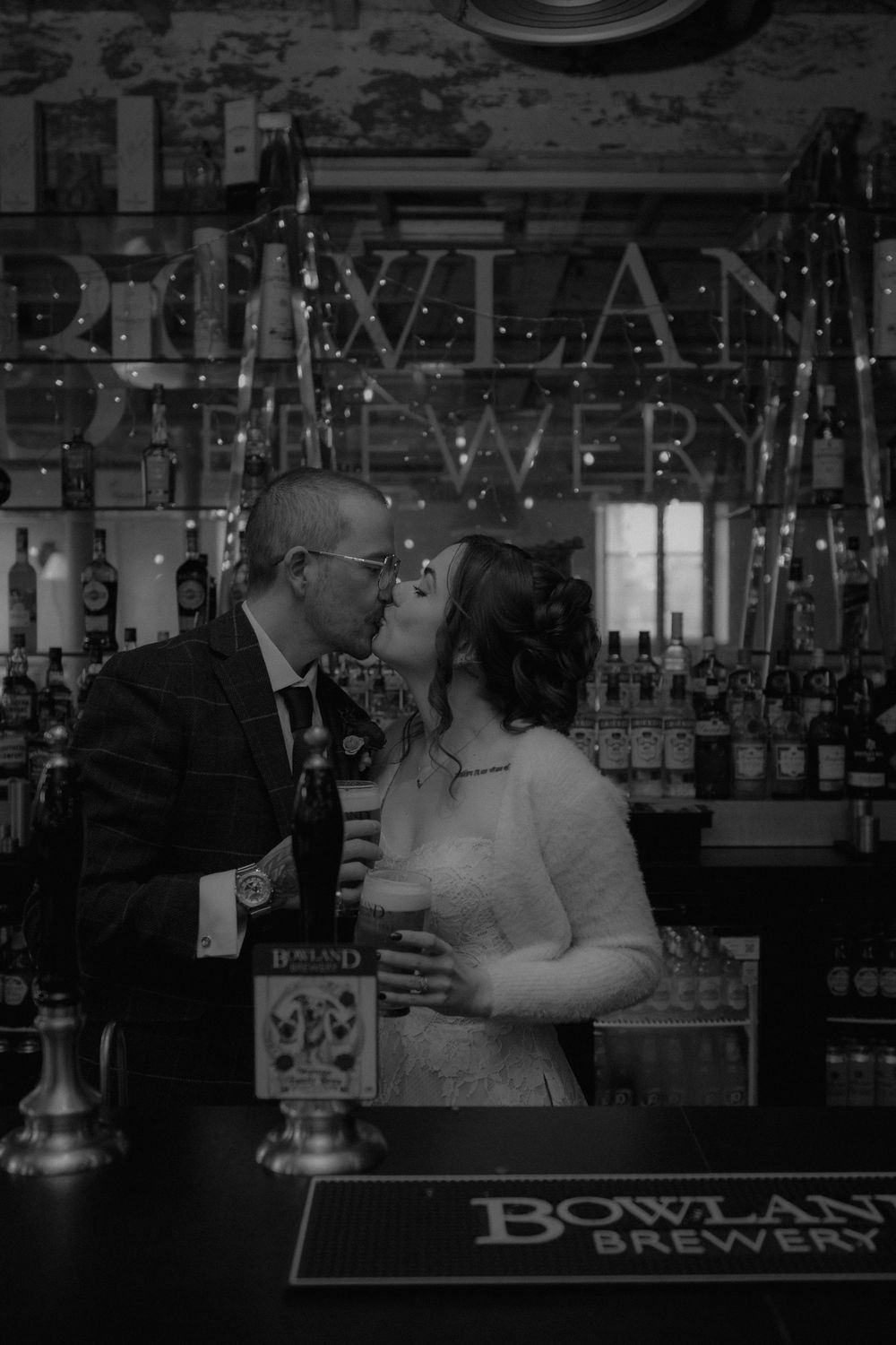 Bride and groom share a kiss at Bowland Brewery bar in a romantic black and white wedding photo.
