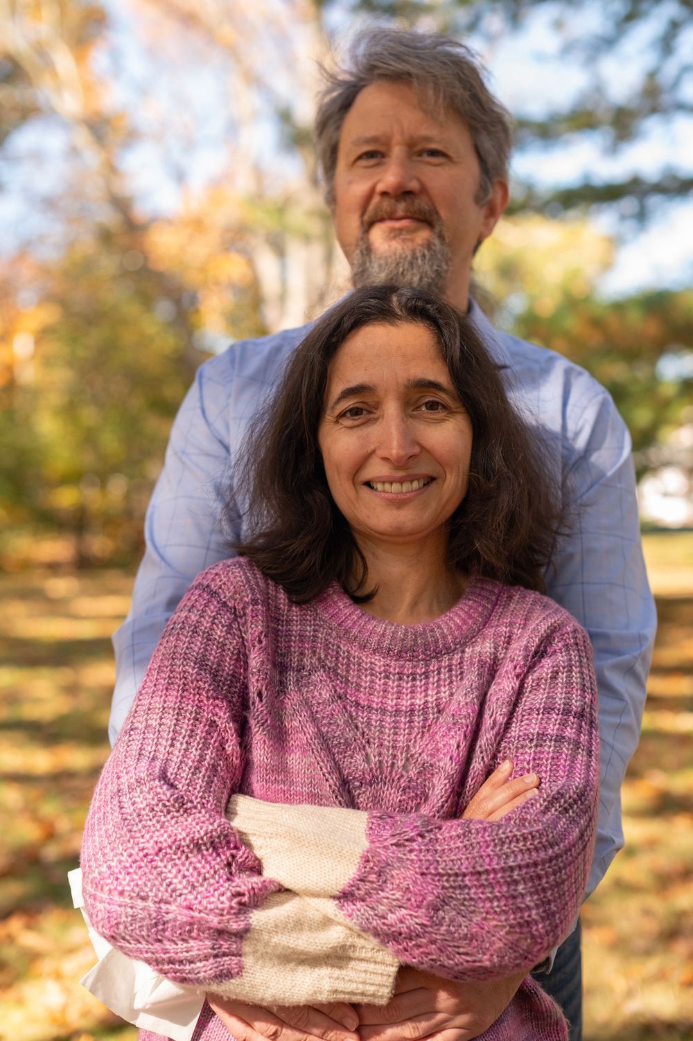 A couple embraces outdoors during golden hour autumn light wearing a pink knit sweater.