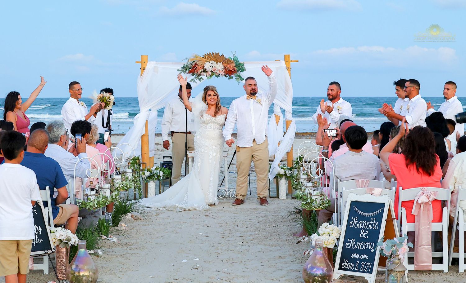 A beach wedding ceremony setup with white chairs and floral decorations along a sandy aisle leading to the ocean.