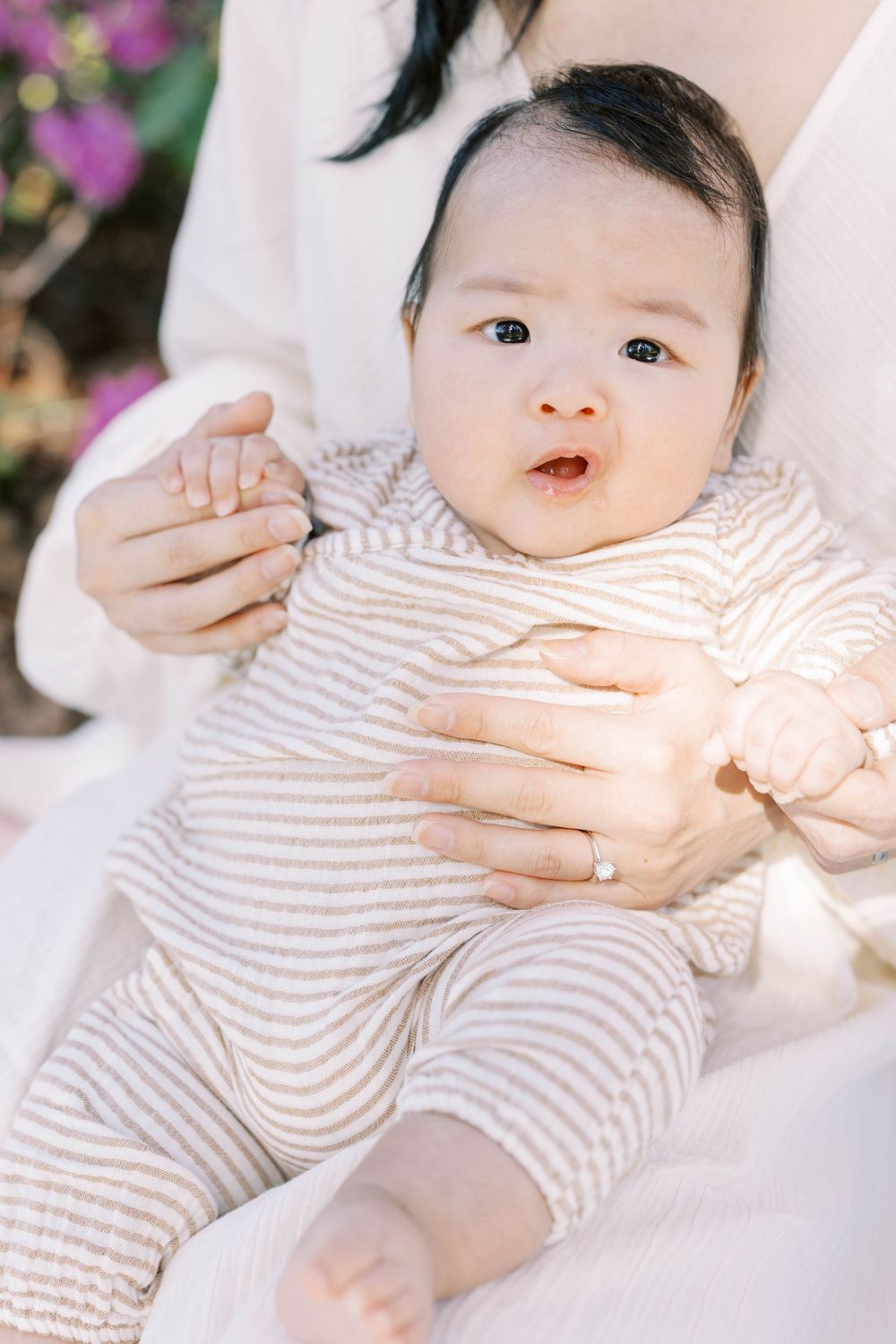 Close-up of newborn baby in striped onesie being held by mother wearing diamond engagement ring.