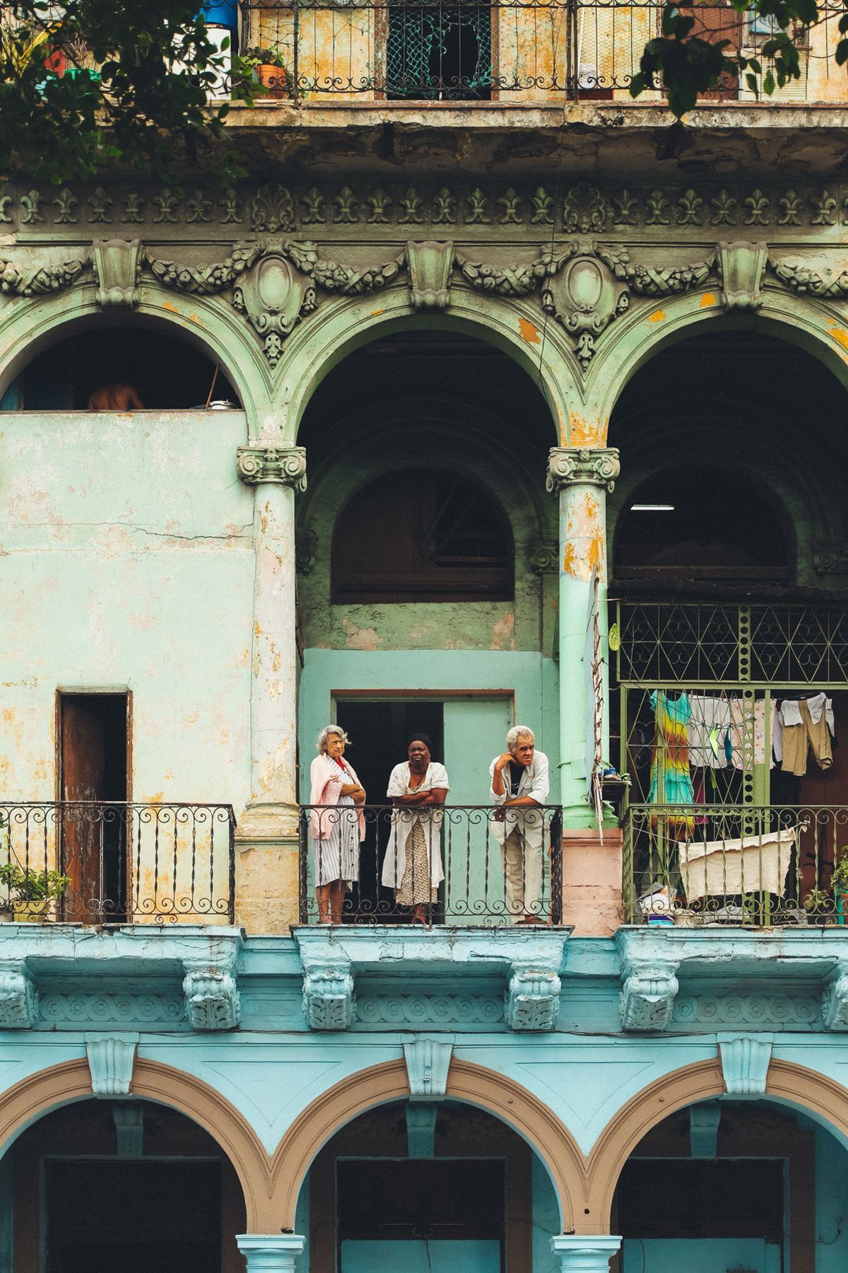 People on ornate colonial balcony with arched architecture in pastel blue and white.