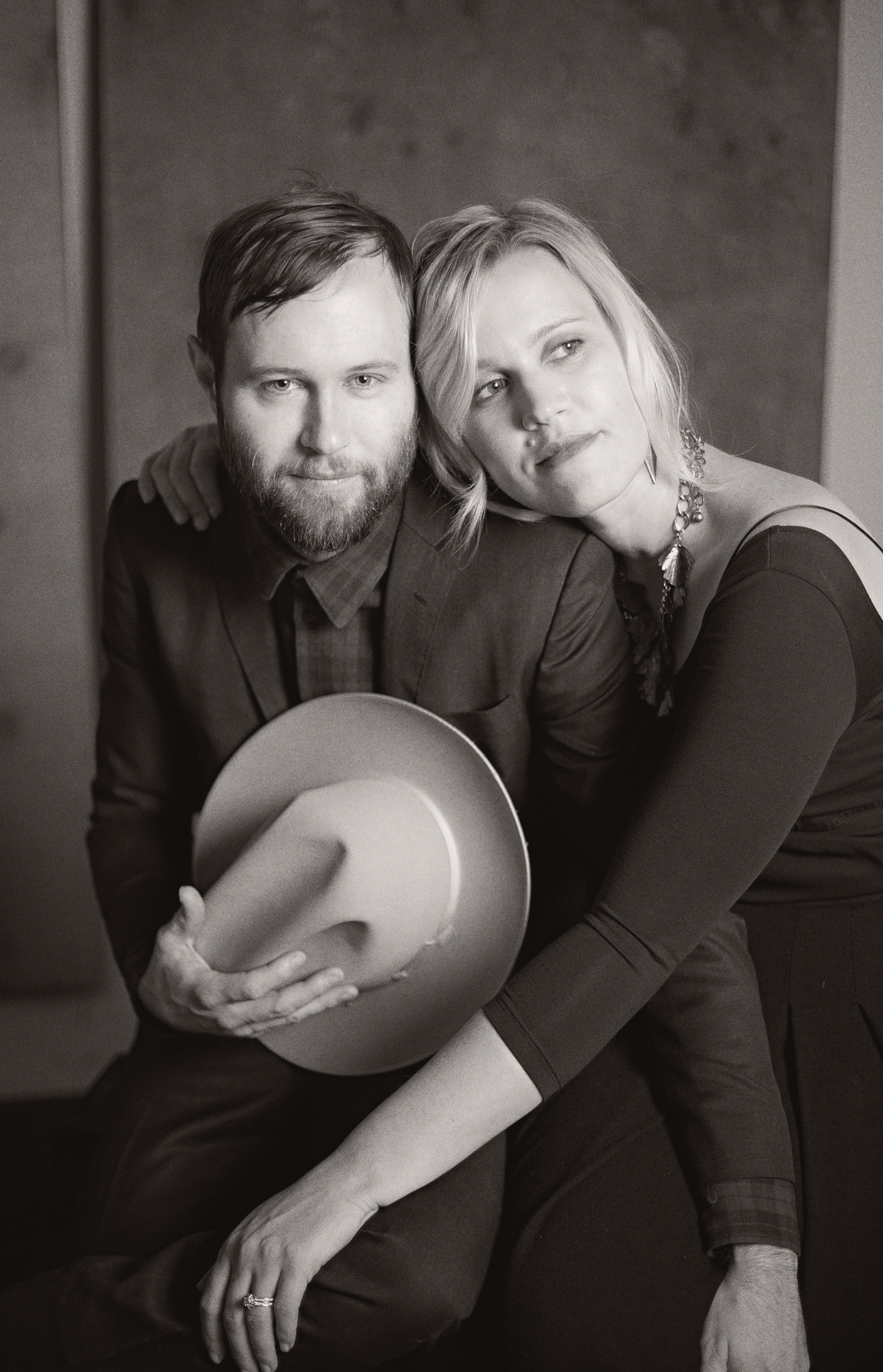 Black and white portrait of a couple in dark clothing posing together with a cowboy hat.