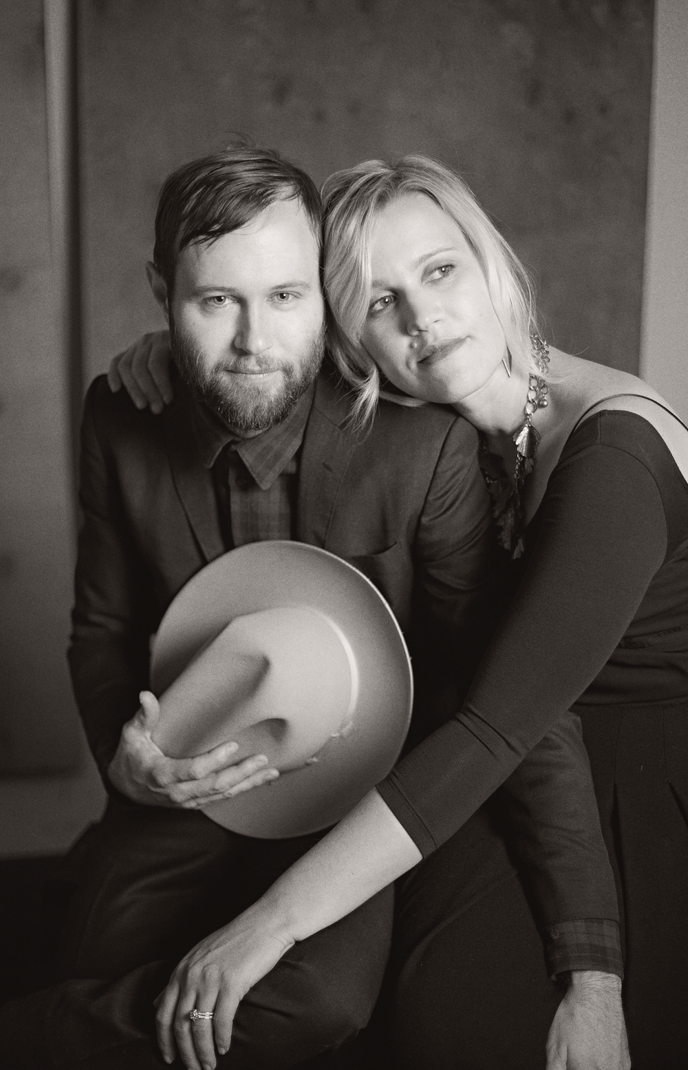 Black and white portrait of a couple in dark clothing posing together with a cowboy hat.