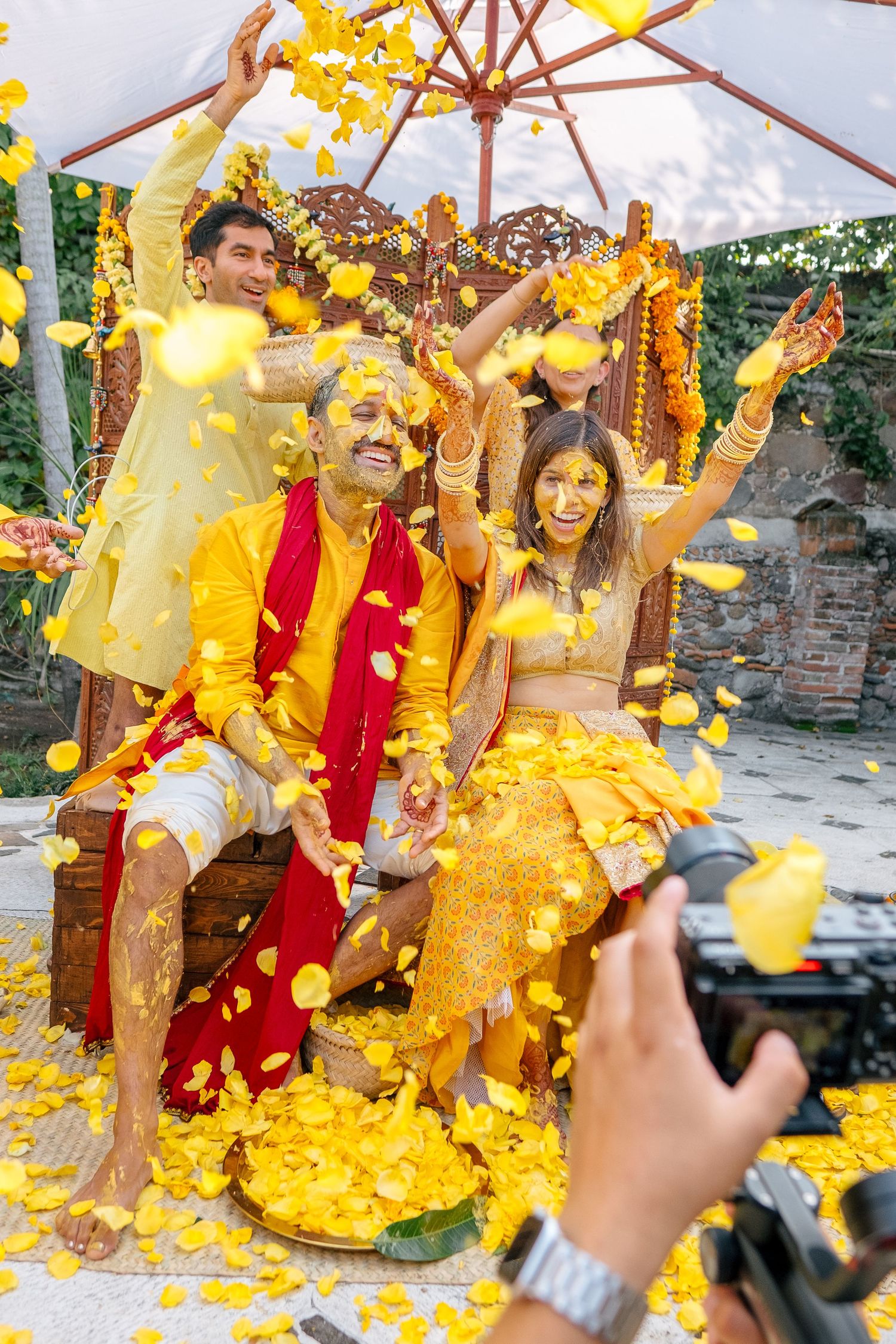 Joyful celebration with yellow flower petals showering over couple under umbrella.