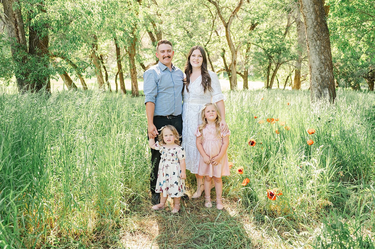 Family of four poses together in a scenic woodland setting with orange poppies.