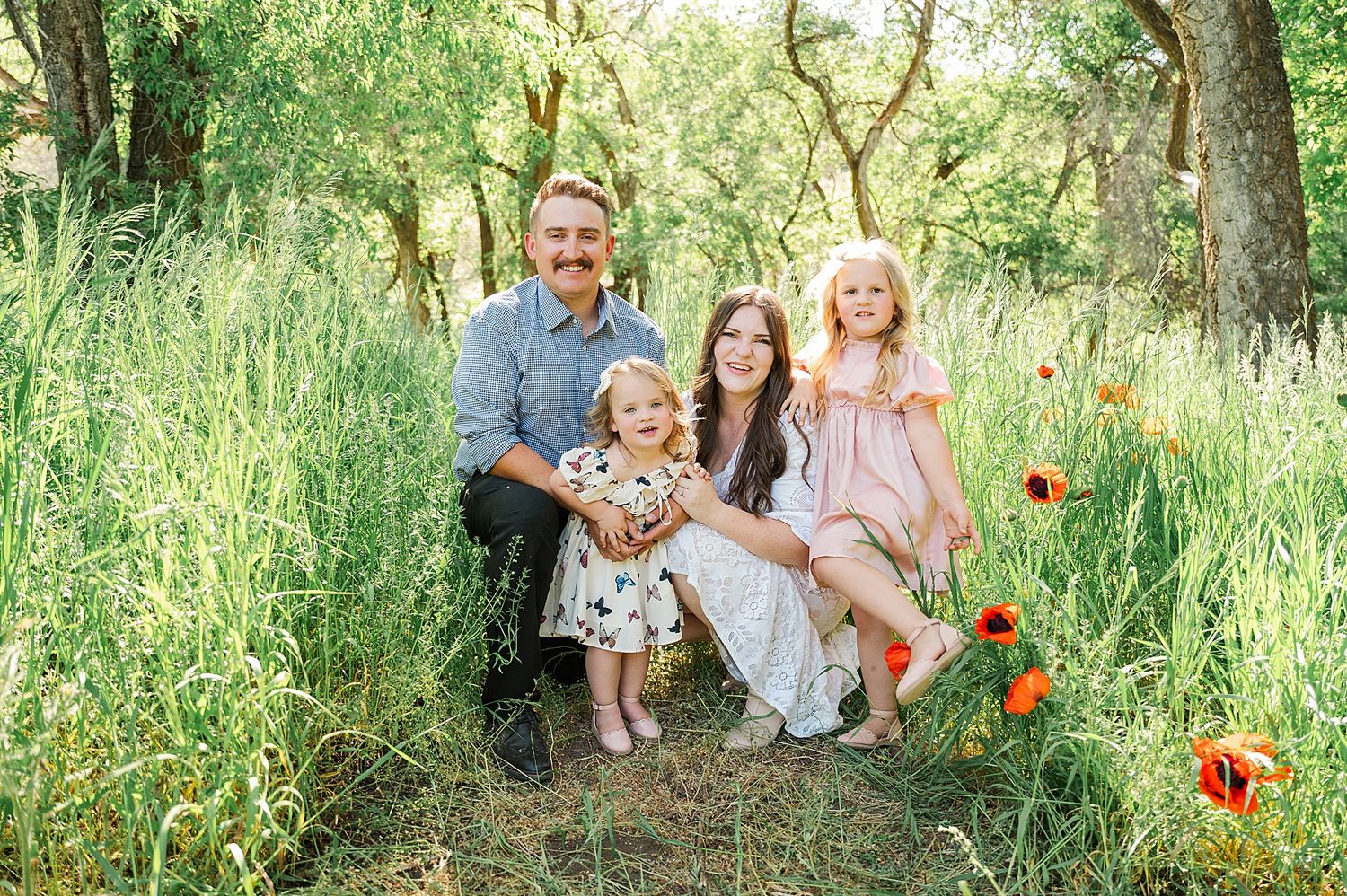 Family group sitting together on grass surrounded by blooming orange poppies and trees.