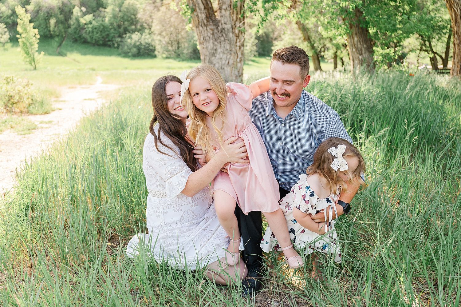 A family shares a joyful moment together on grassy hillside during golden hour photo session.