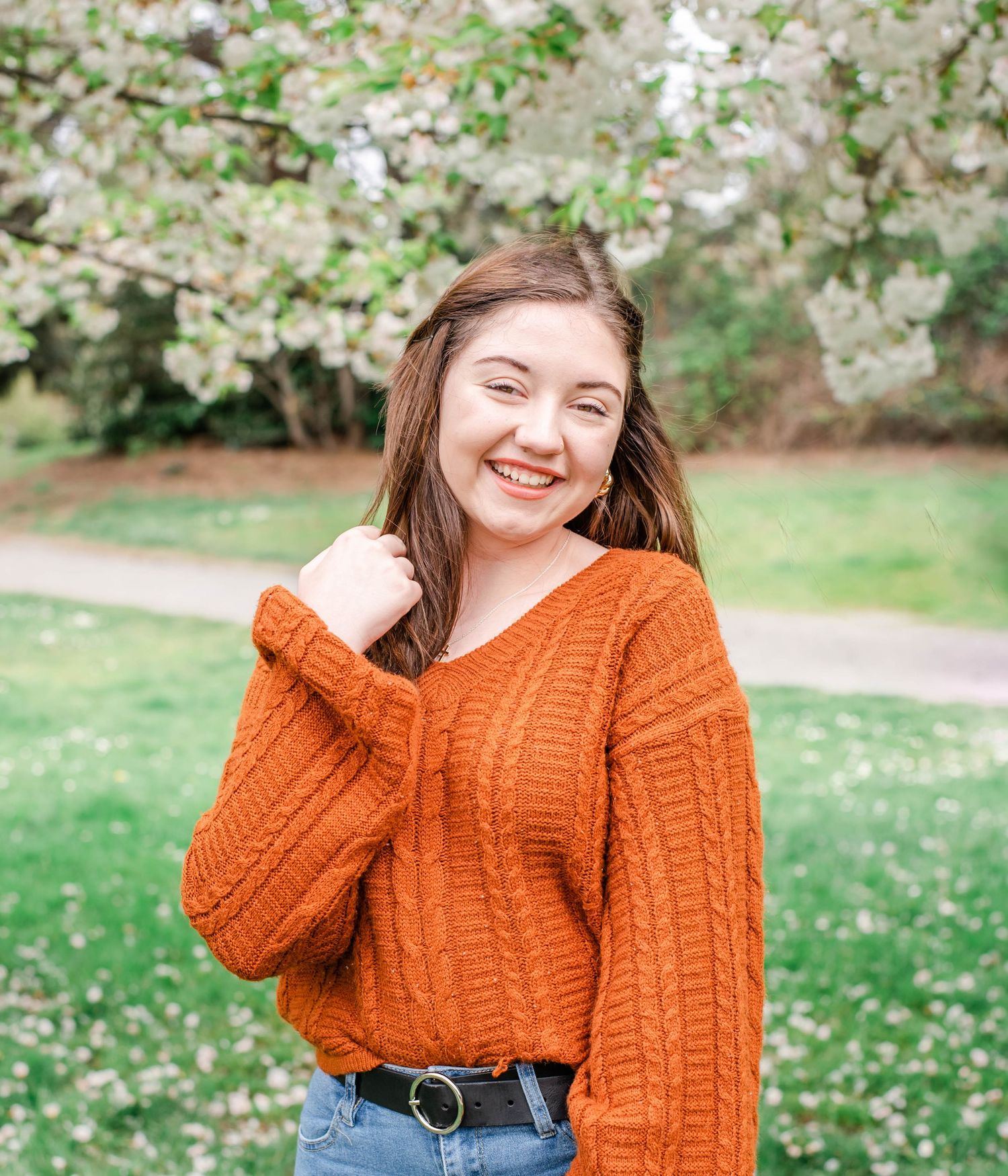 Cozy orange knit sweater styled with denim jeans against floral spring backdrop.