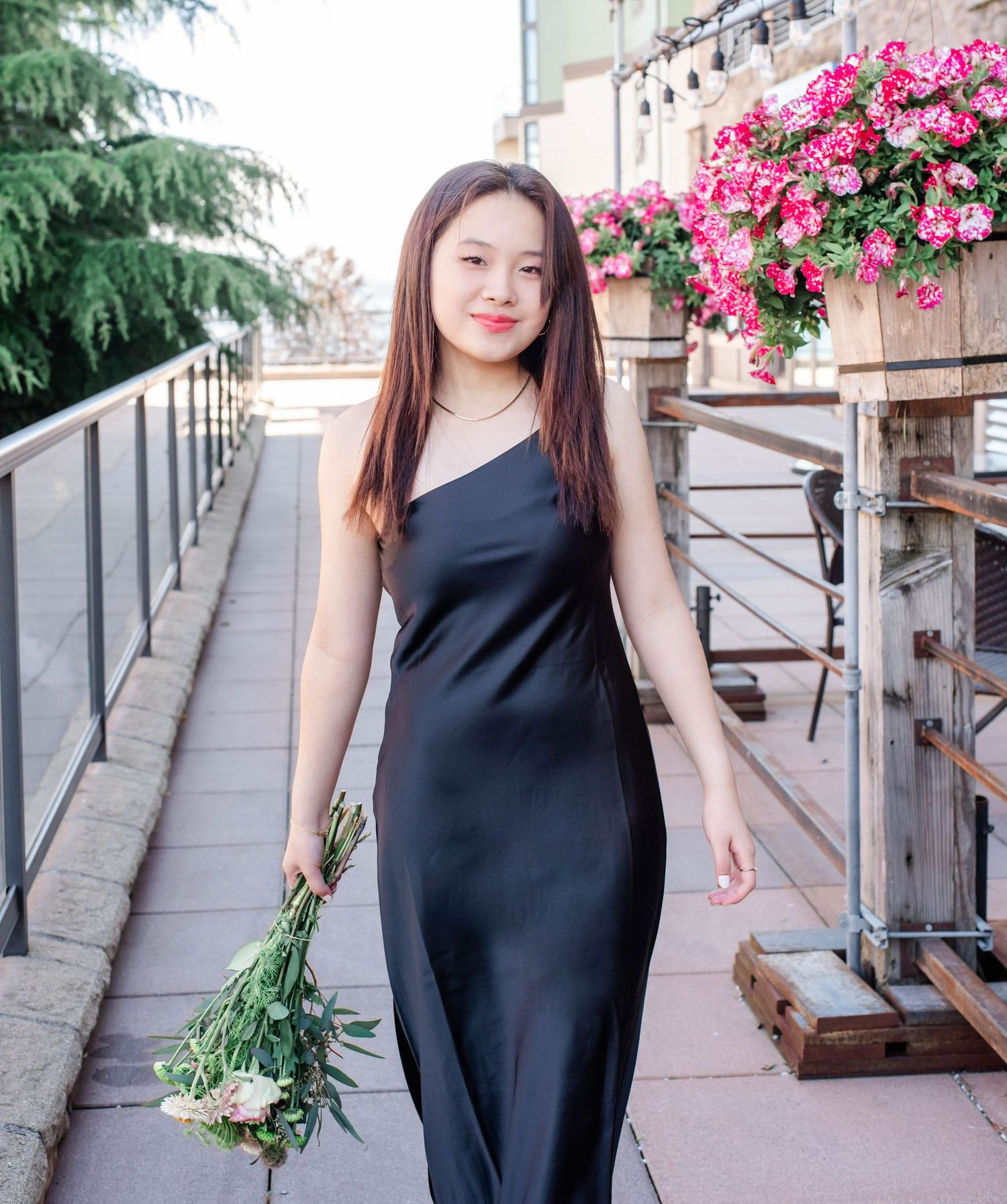 Stylish black sleeveless dress worn against a backdrop of vibrant pink flowers and green foliage.