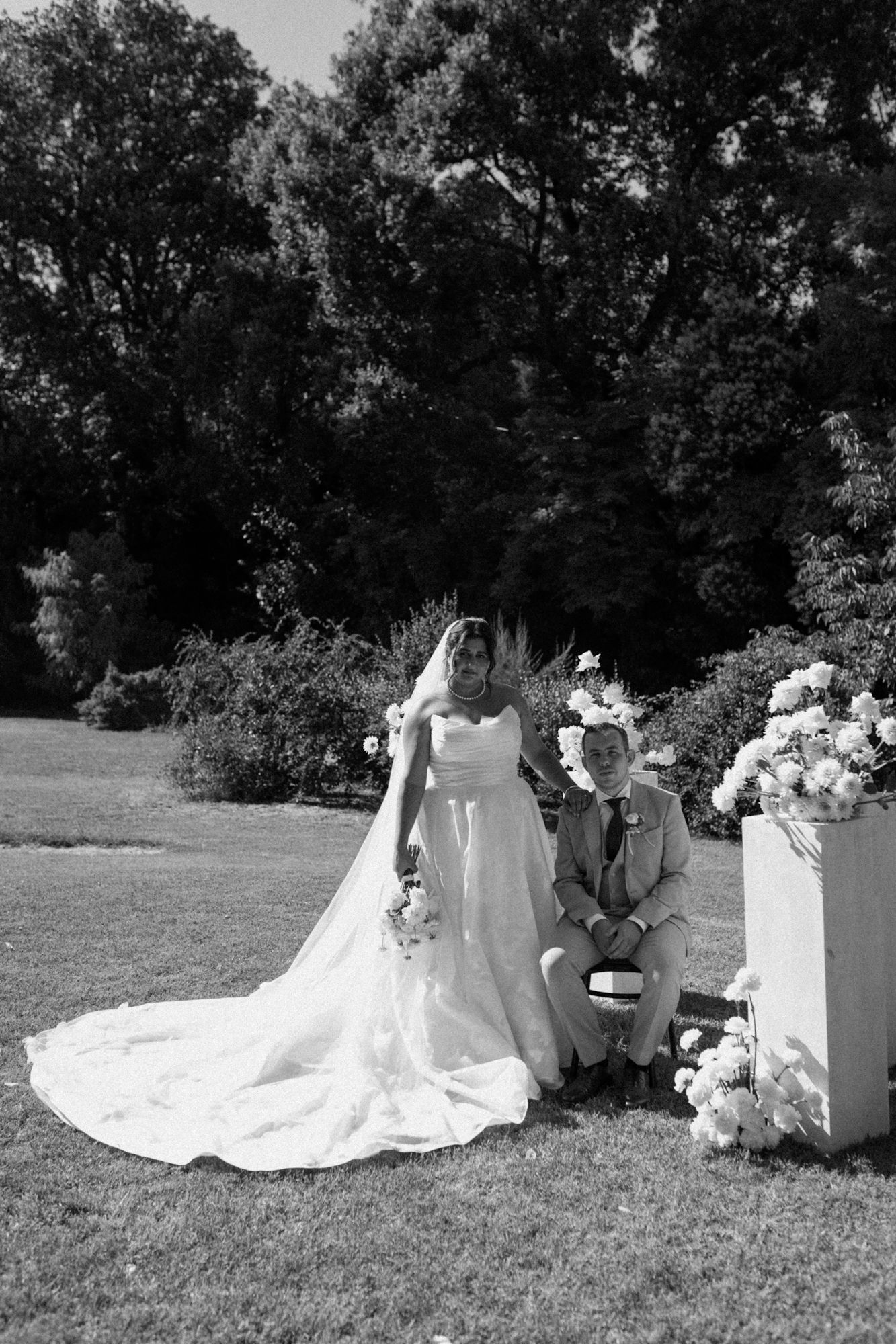 Wedding photo of a bride and groom sitting with white floral arrangements at an outdoor destination wedding in Fano, Marche Italy.