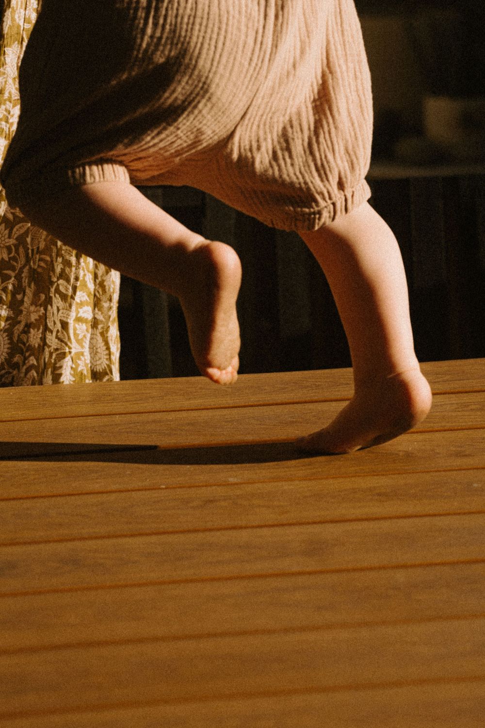 Close-up shots of small bare feet walking across a wooden floor in warm lighting.