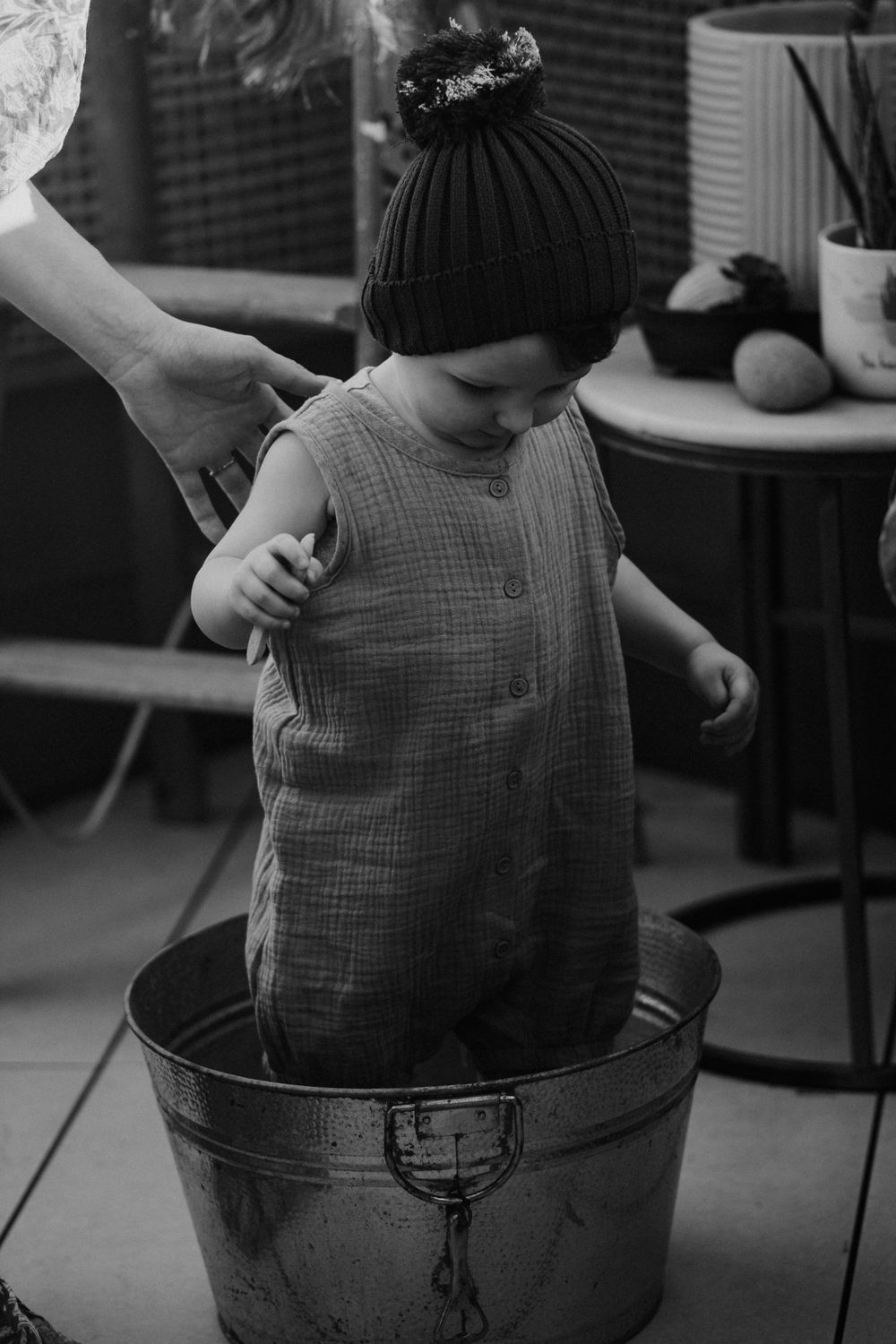 Small child wearing a beanie and romper stands in a metal washtub during playtime.