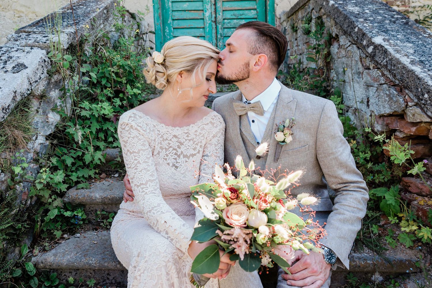 Bride and groom sitting on top of a staircase and groom is lovinly kissing the brides forehead