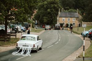 Classic white wedding car with tin cans driving down a village road.