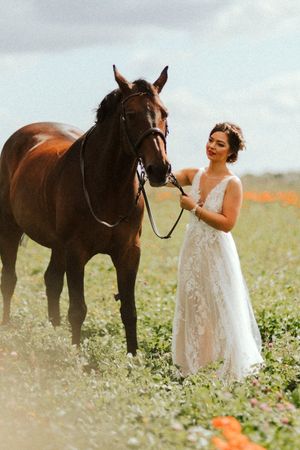 A white dress contrasts beautifully with brown horses in a wildflower meadow during a wedding photoshoot.