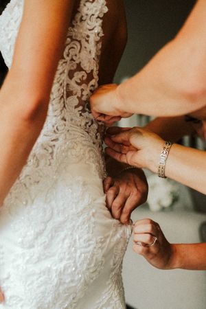 Close-up of intricate lace details being adjusted on white wedding dress.