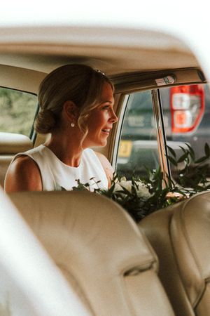 Bride sitting in vintage car with white floral bouquet and elegant hairstyle.