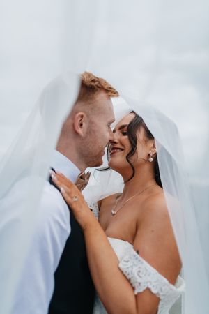 A romantic wedding moment captured under a flowing veil as the couple shares an intimate close embrace.
