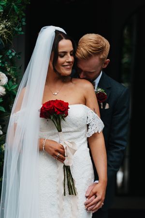 Beautiful wedding sequence shows a bride in lacy white dress holding red roses as she embraces with her partner.