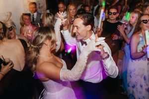 Wedding guests dance and celebrate on a crowded dance floor illuminated by colorful lights at a reception.